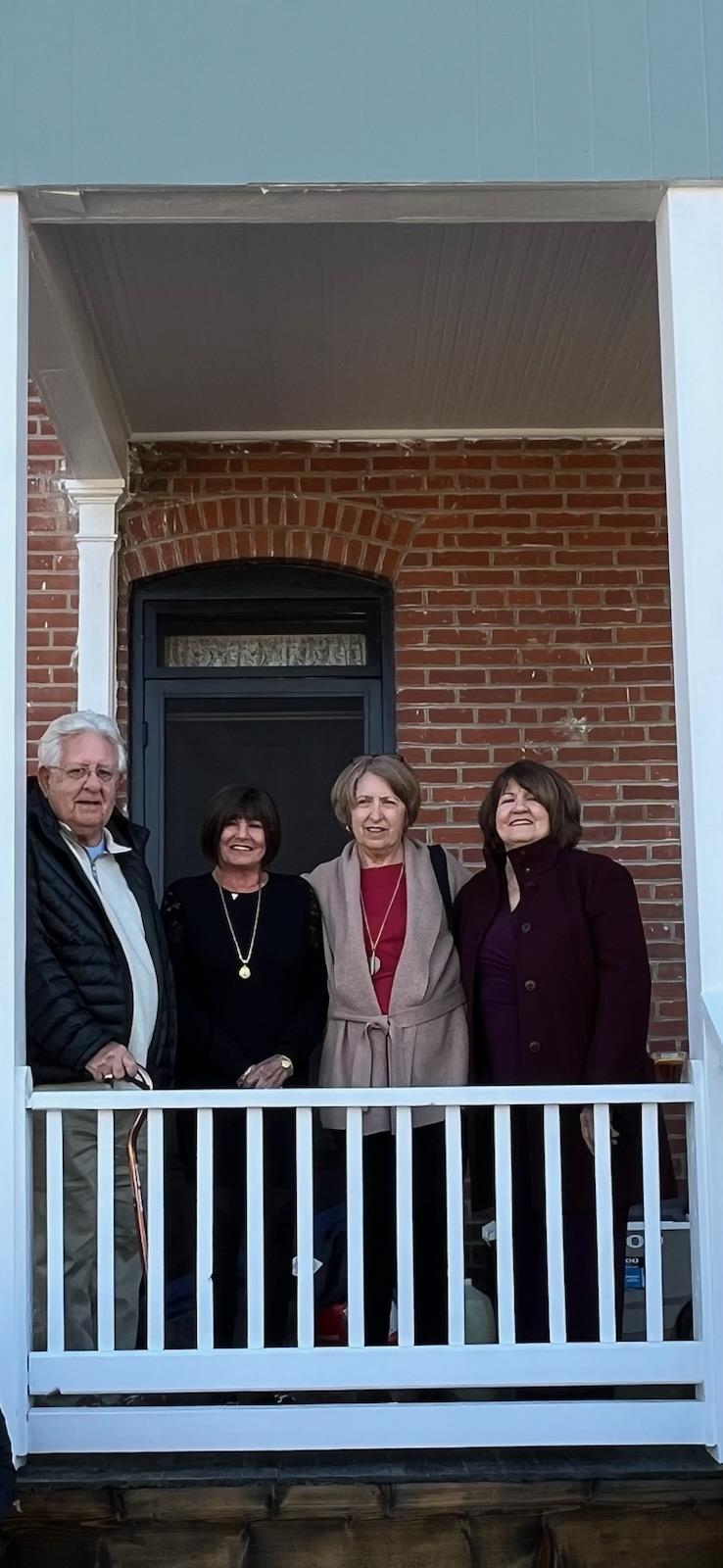 Four family members stand together on a porch, enjoying a pleasant afternoon in front of their home.