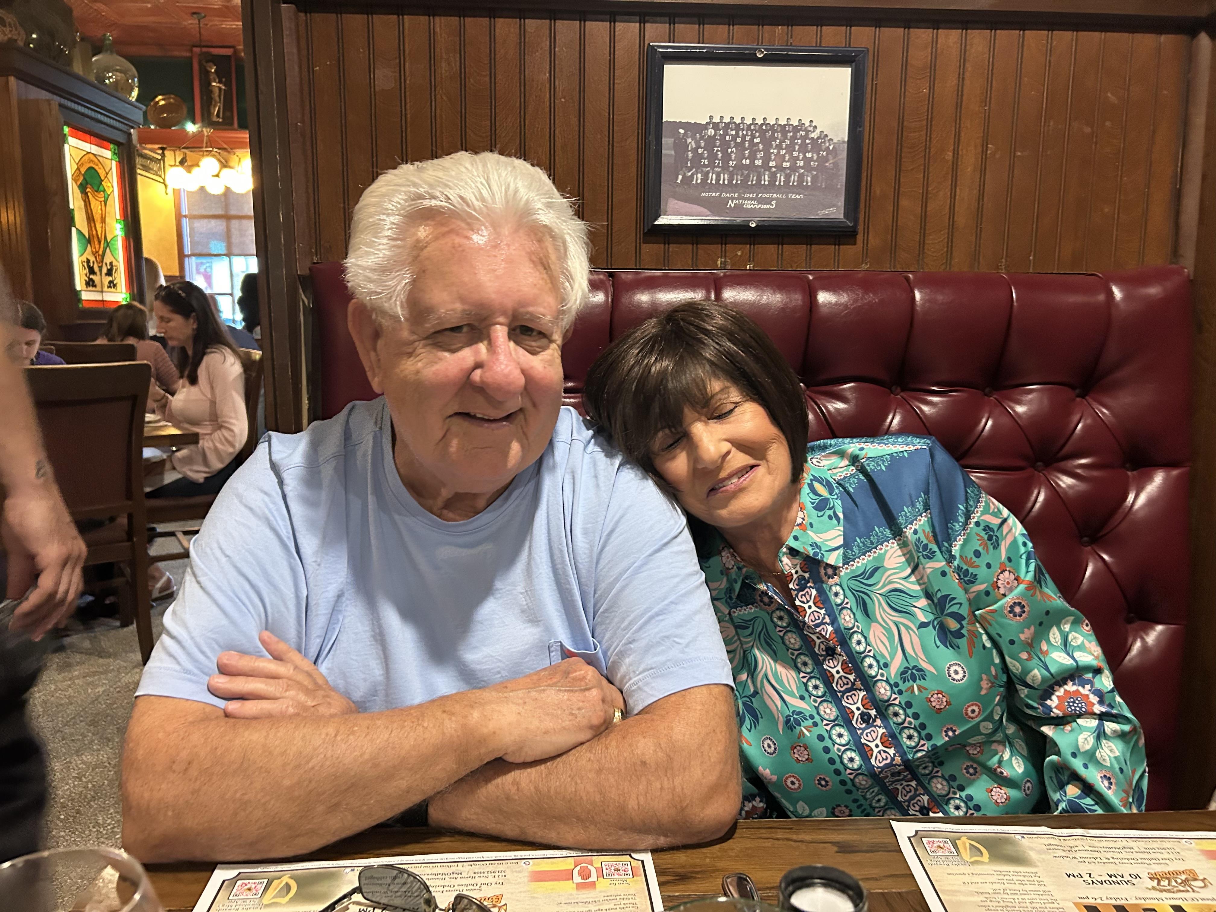 Two individuals share a warm moment, smiling and dining in a restaurant setting.