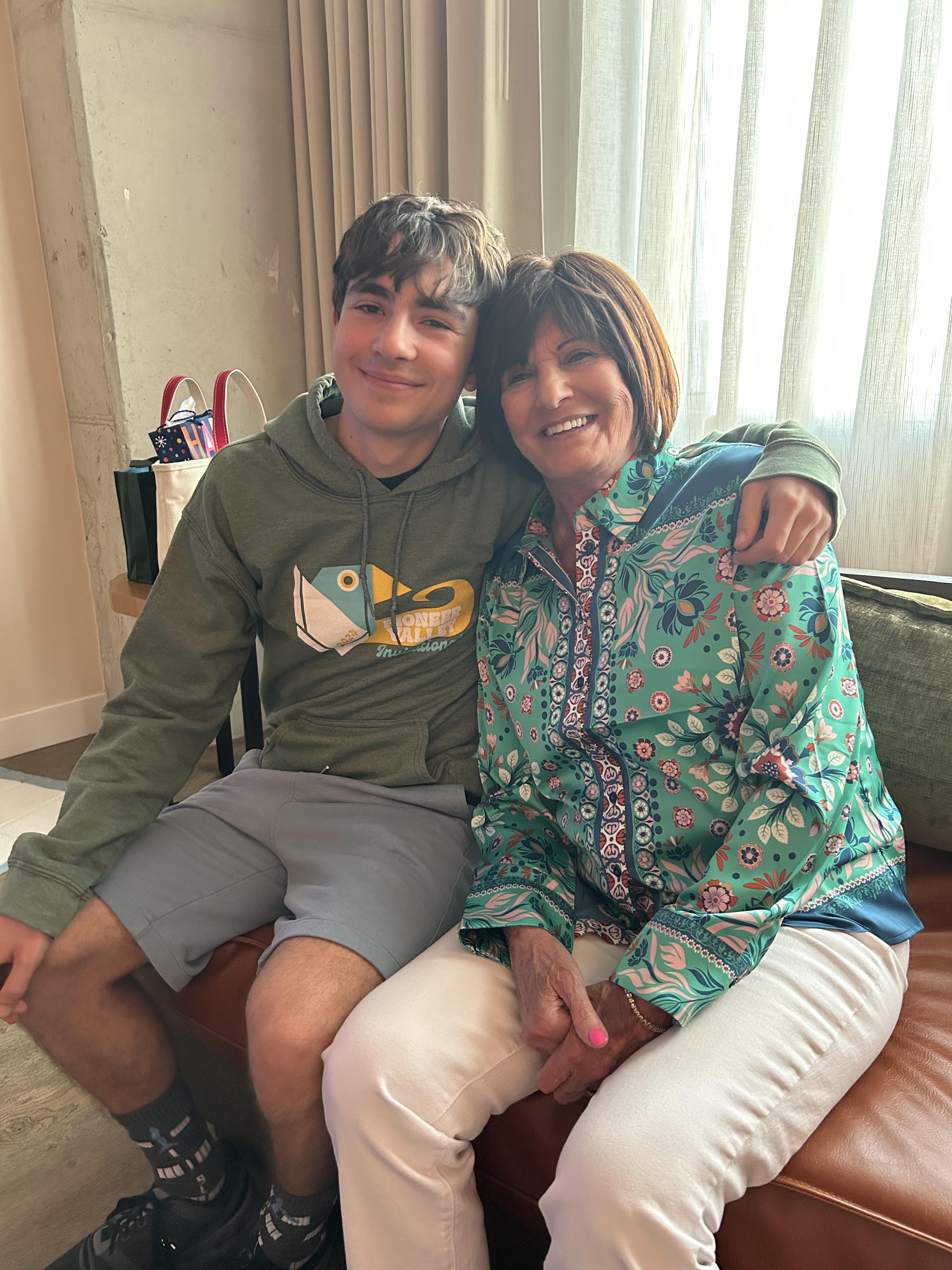 Grandmother and grandson share a joyful embrace while sitting on a couch in a warm interior.