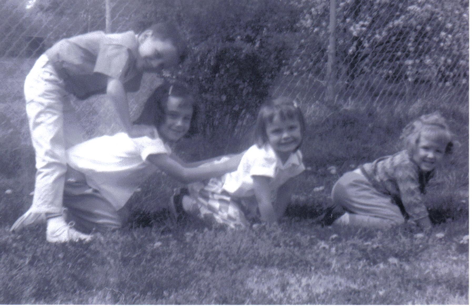 Four children engage in playful activities outdoors, enjoying a sunny day in the grass.