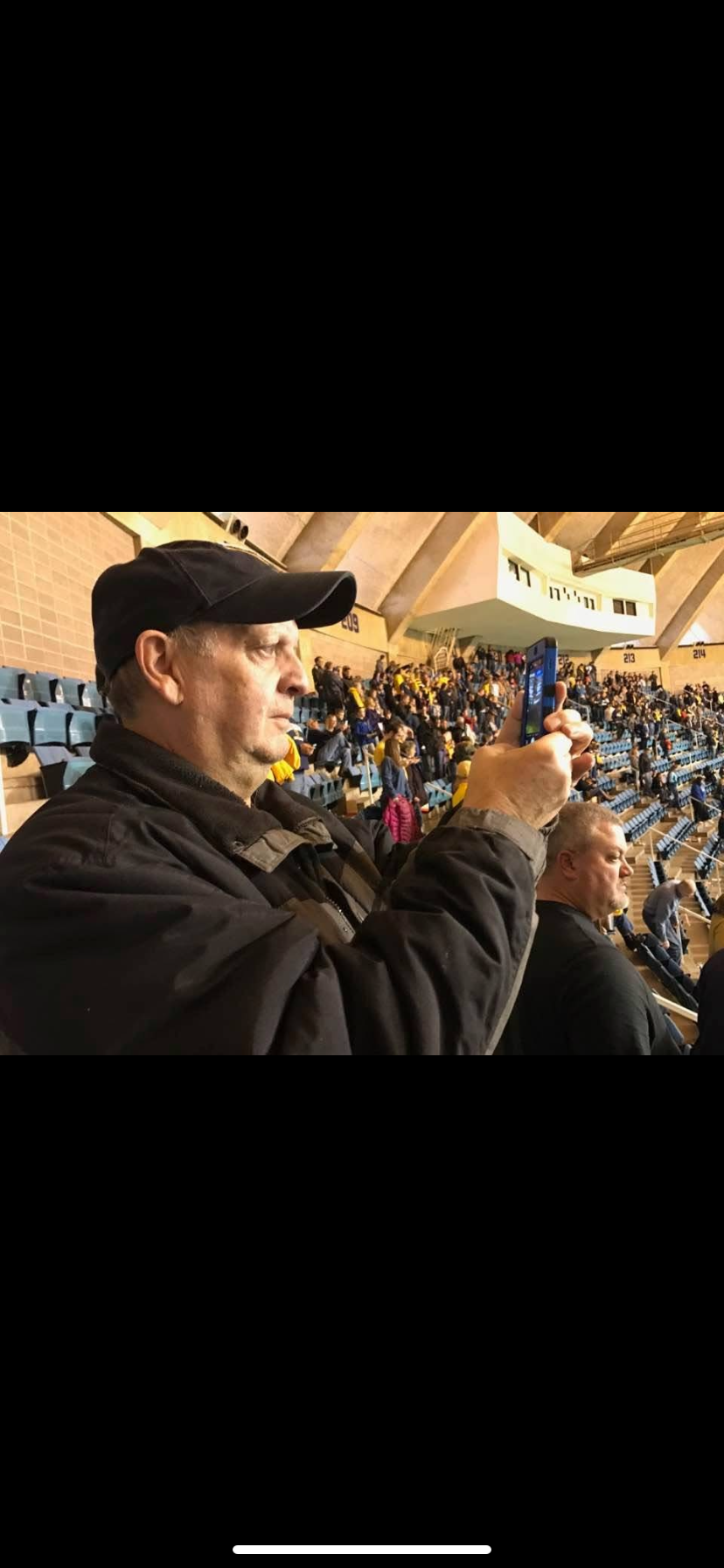 Excited supporter takes pictures during a sports match surrounded by cheering fans.