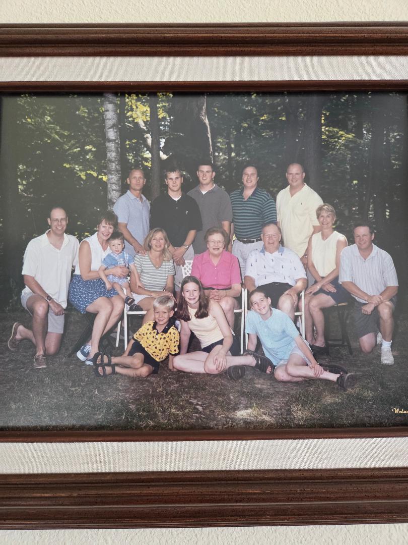 A large family smiles for a portrait outdoors, surrounded by trees.
