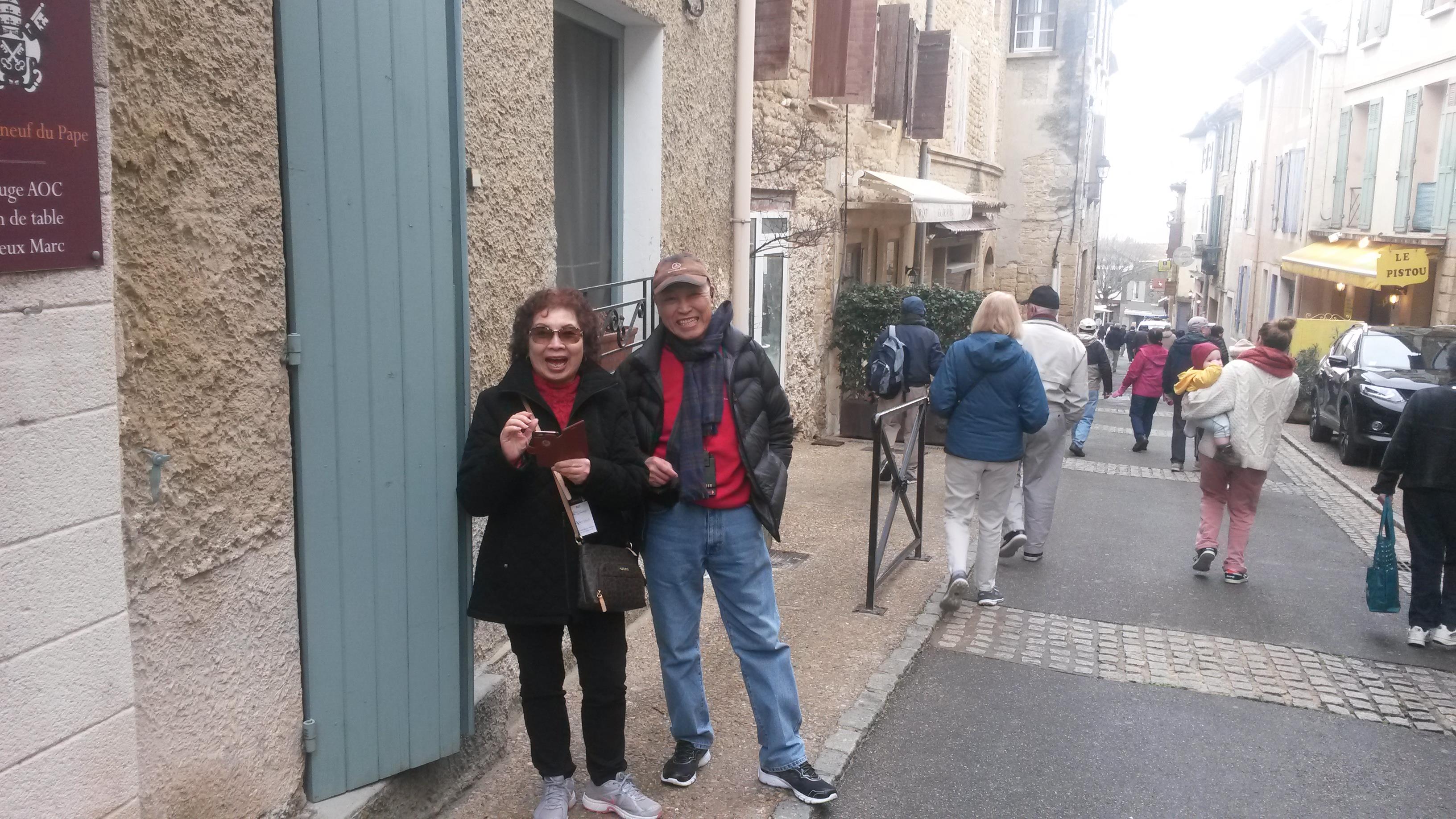 A happy couple poses together on a street lined with quaint shops and pedestrians.