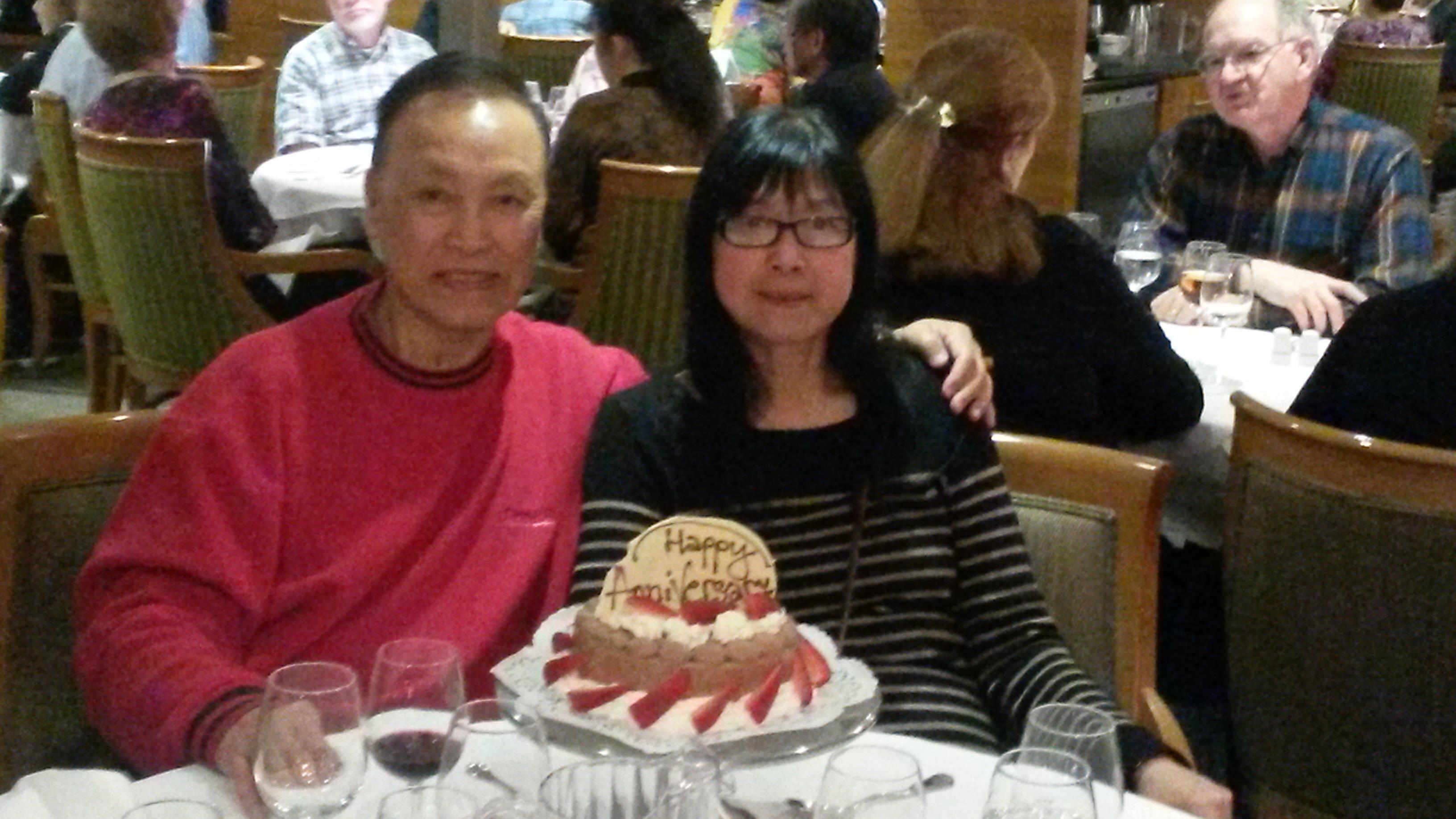 A couple enjoys an anniversary celebration at a lively restaurant with friends and cake.