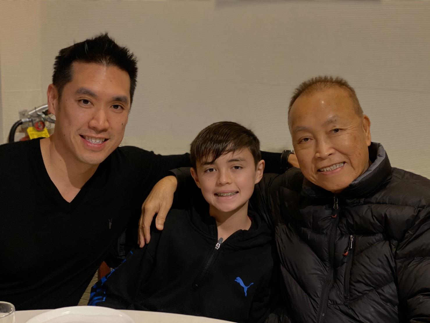 Three family members sit together, smiling warmly in a restaurant setting during dinner.