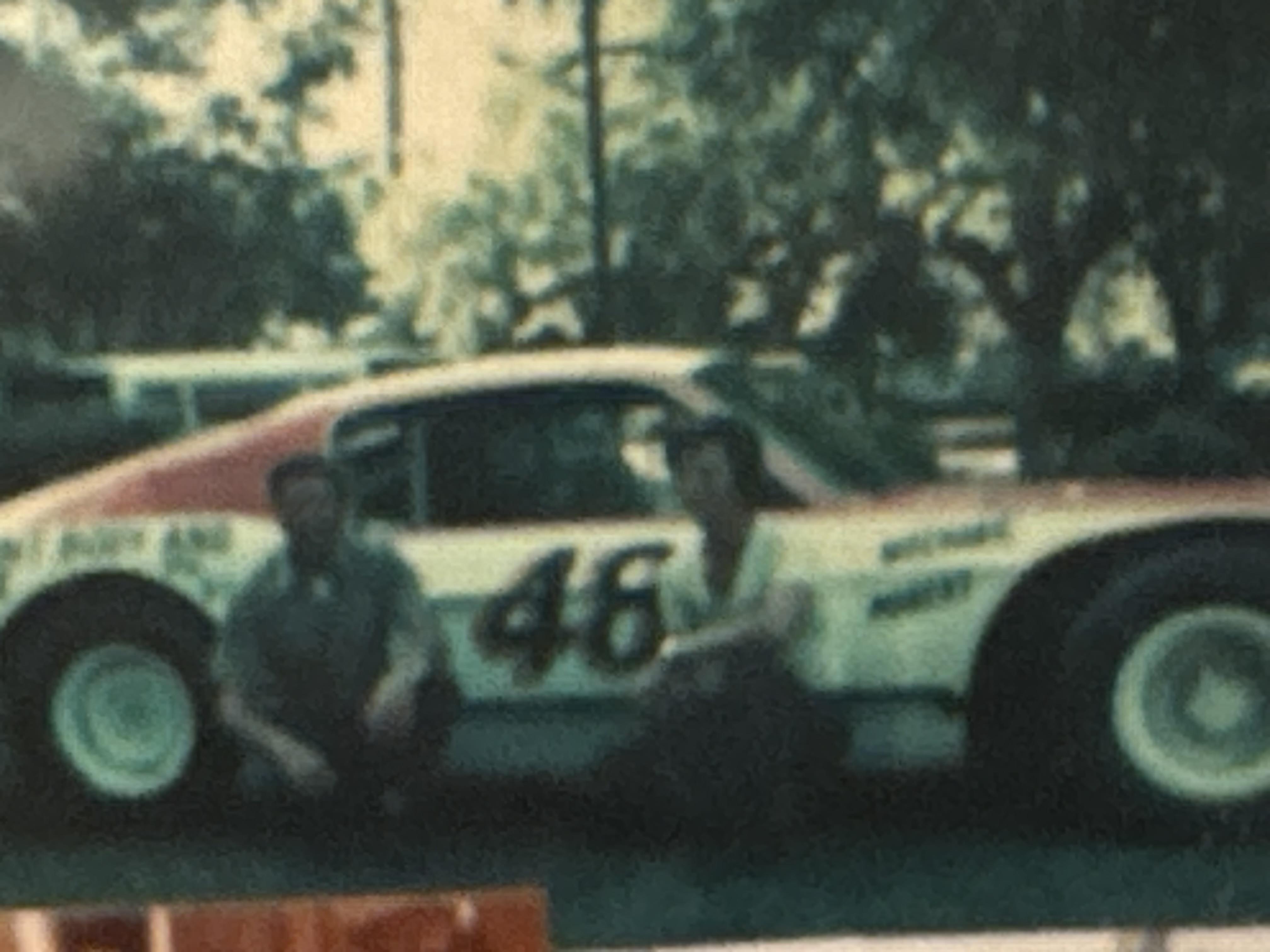 Two individuals kneel beside a classic race car, showcasing their passion for motorsports.