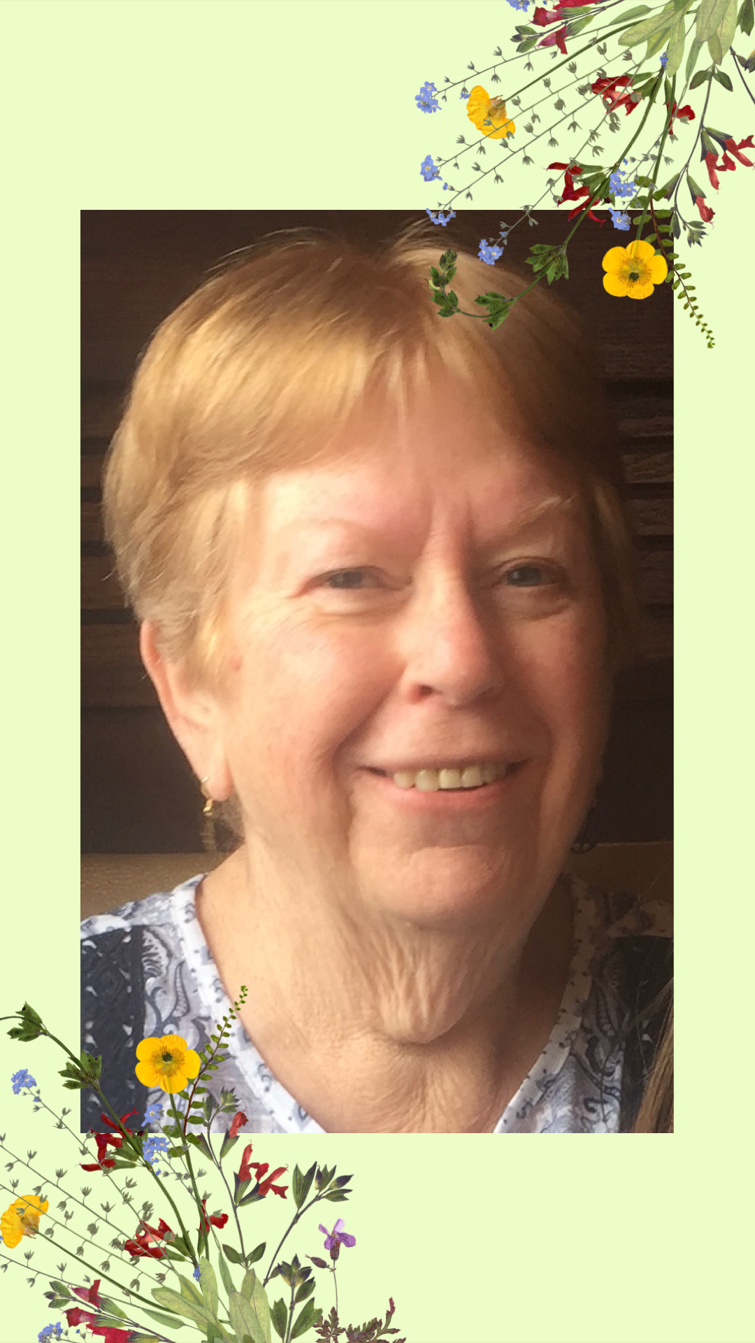 A cheerful elderly woman with light hair smiles at the camera, exuding warmth and friendliness.