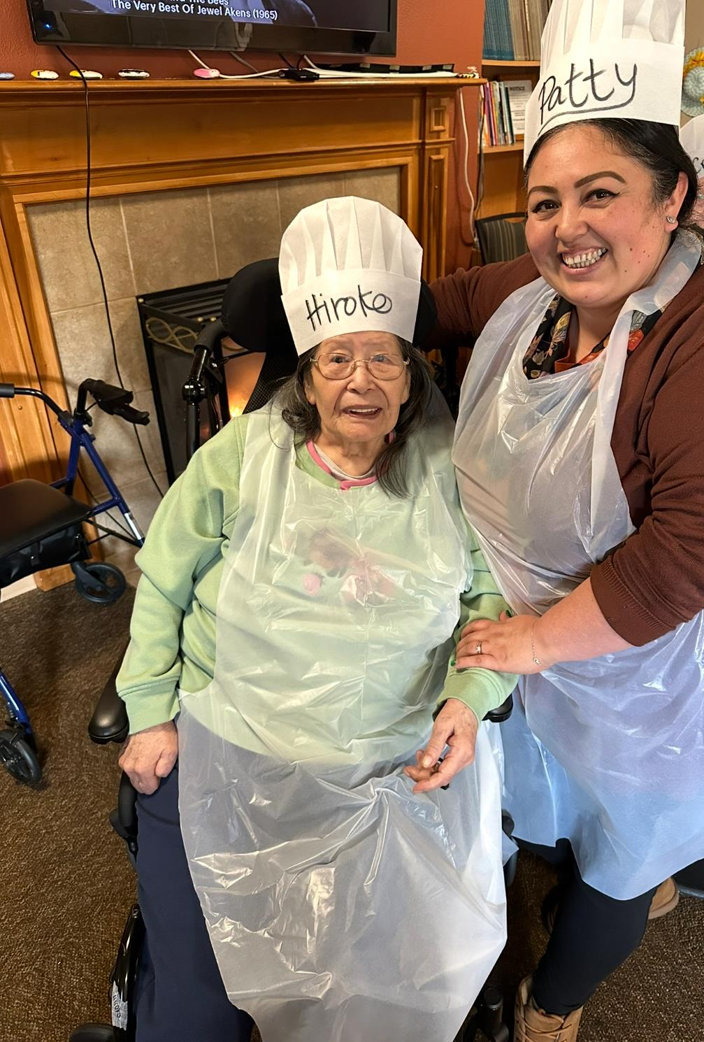 Residents participate in a joyful cooking activity while wearing chef hats and aprons.