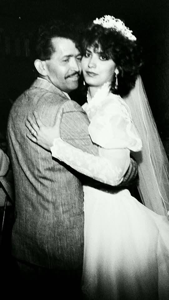 A couple dances closely, wearing elegant wedding attire, surrounded by a festive atmosphere.
