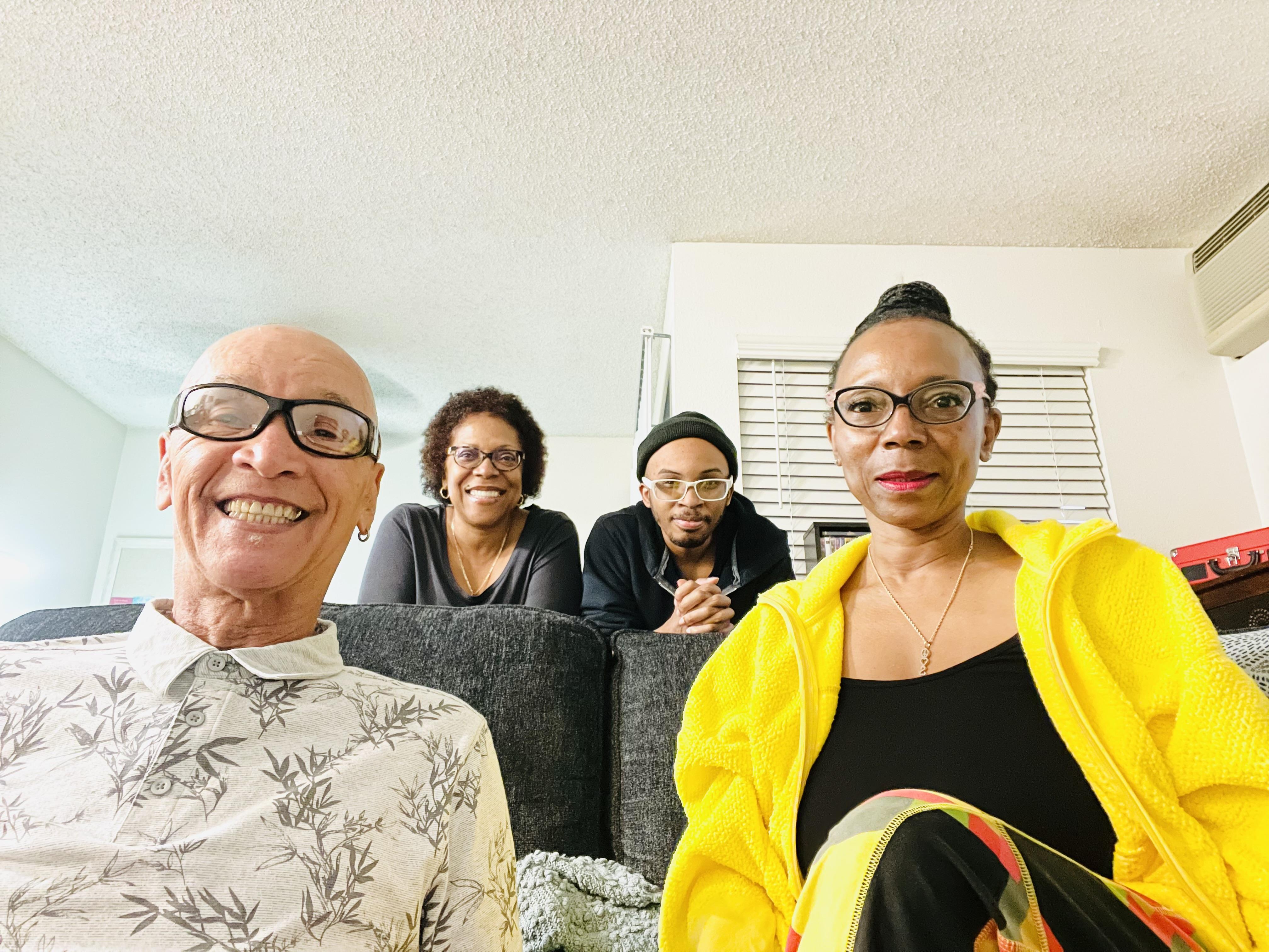 Four adults smiling together in a cozy living room with colorful attire, displaying unity and joy.
