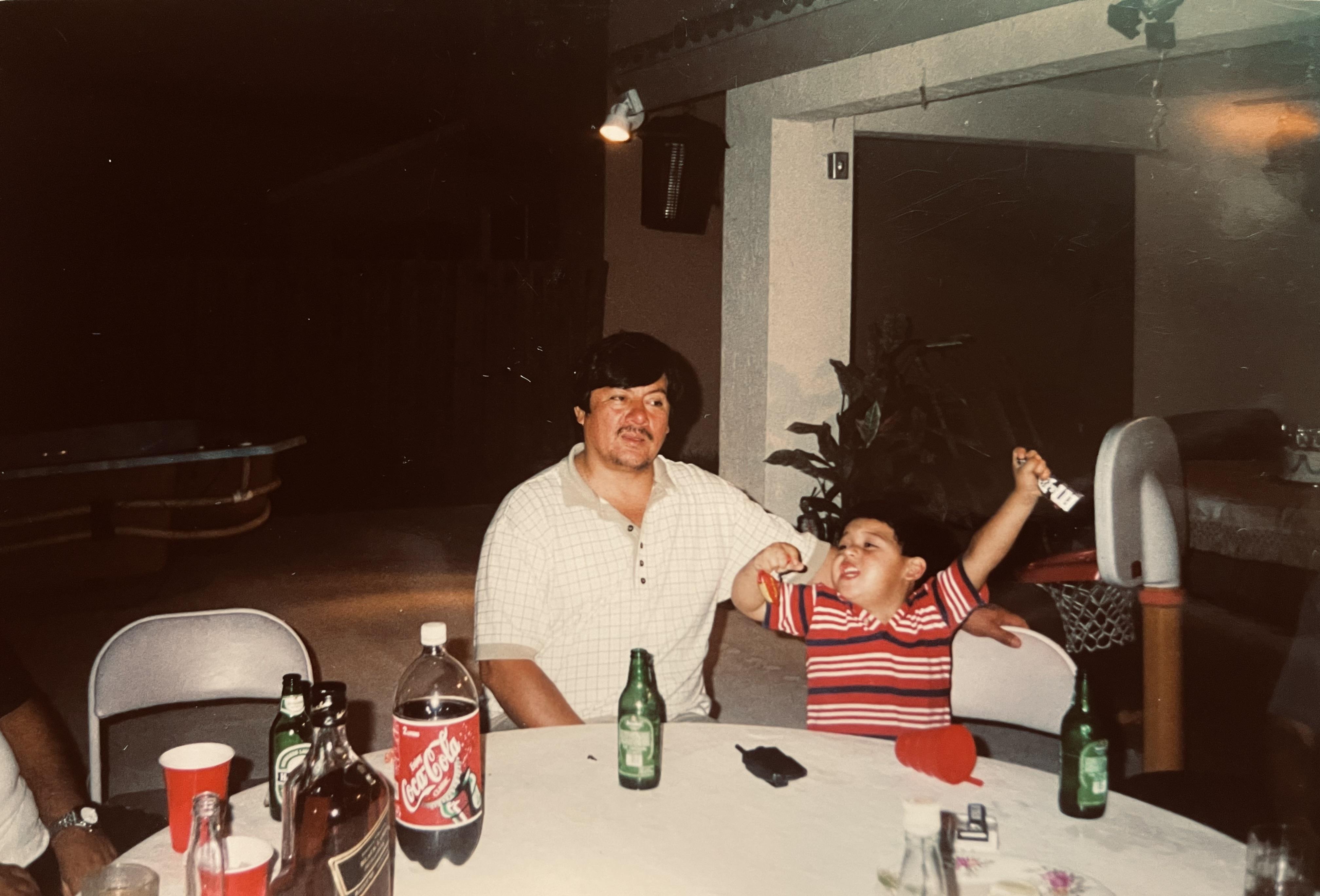 A man and child sitting at a table with soda bottles