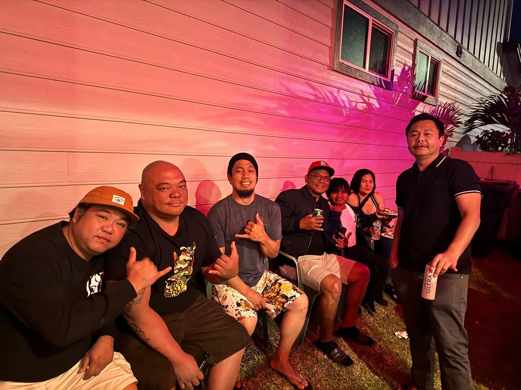 Friends relaxed and chatted under colorful lights in a backyard, sharing drinks and laughs.