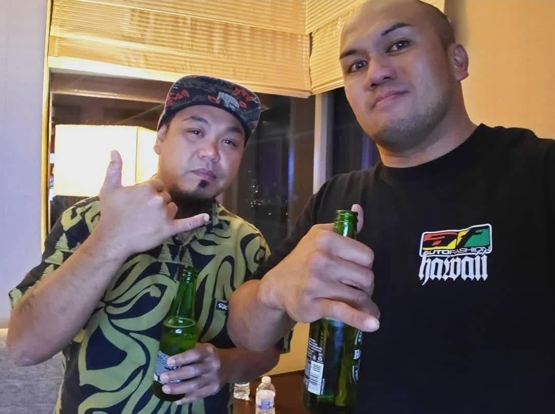 Two friends pose with drinks, smiling in a cozy hotel room filled with city lights.