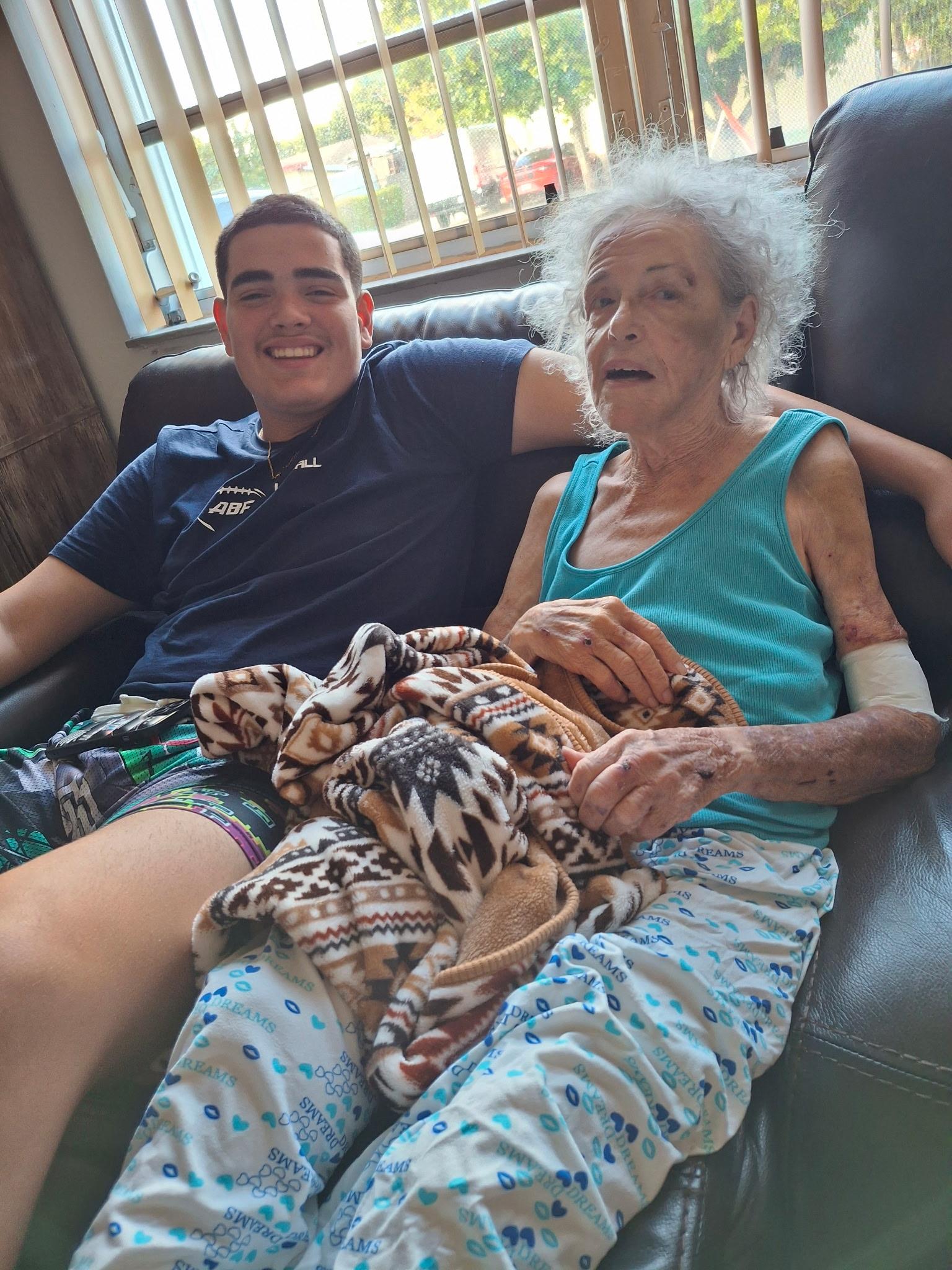 Two relatives smile together while sitting on a couch, wrapped in a blanket, enjoying their time.