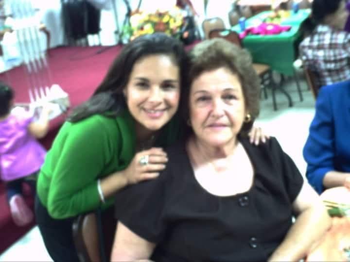 A woman poses happily with her grandmother during a family celebration at a community center.