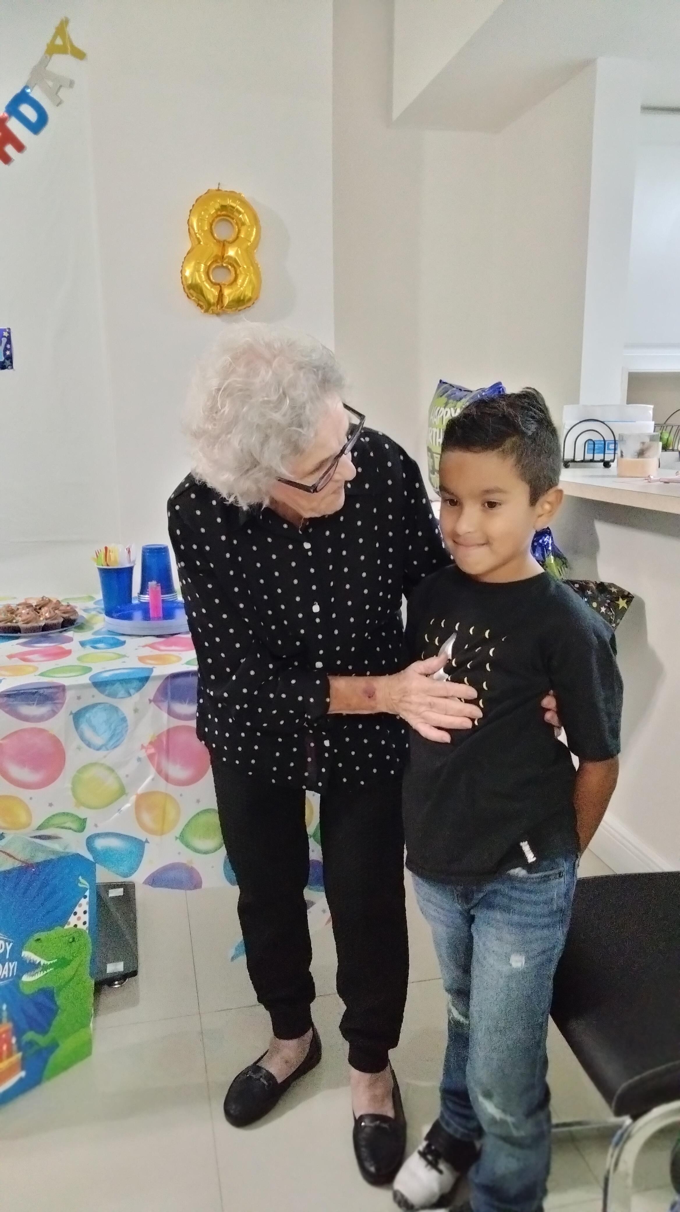 An elderly woman shares a loving moment with a boy at a decorated birthday party.