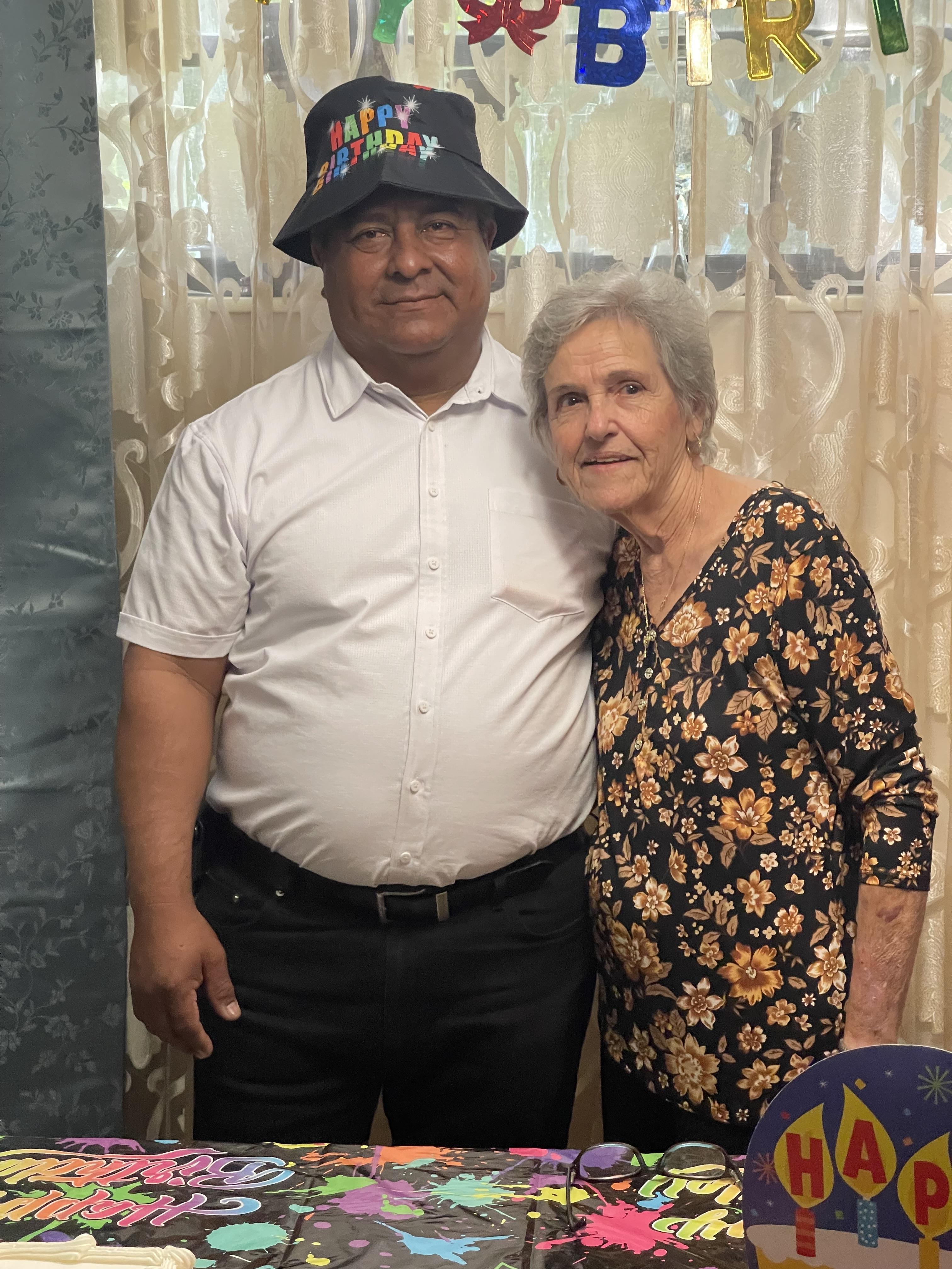 A man and an elderly woman smile at a vibrant birthday celebration with colorful decor.