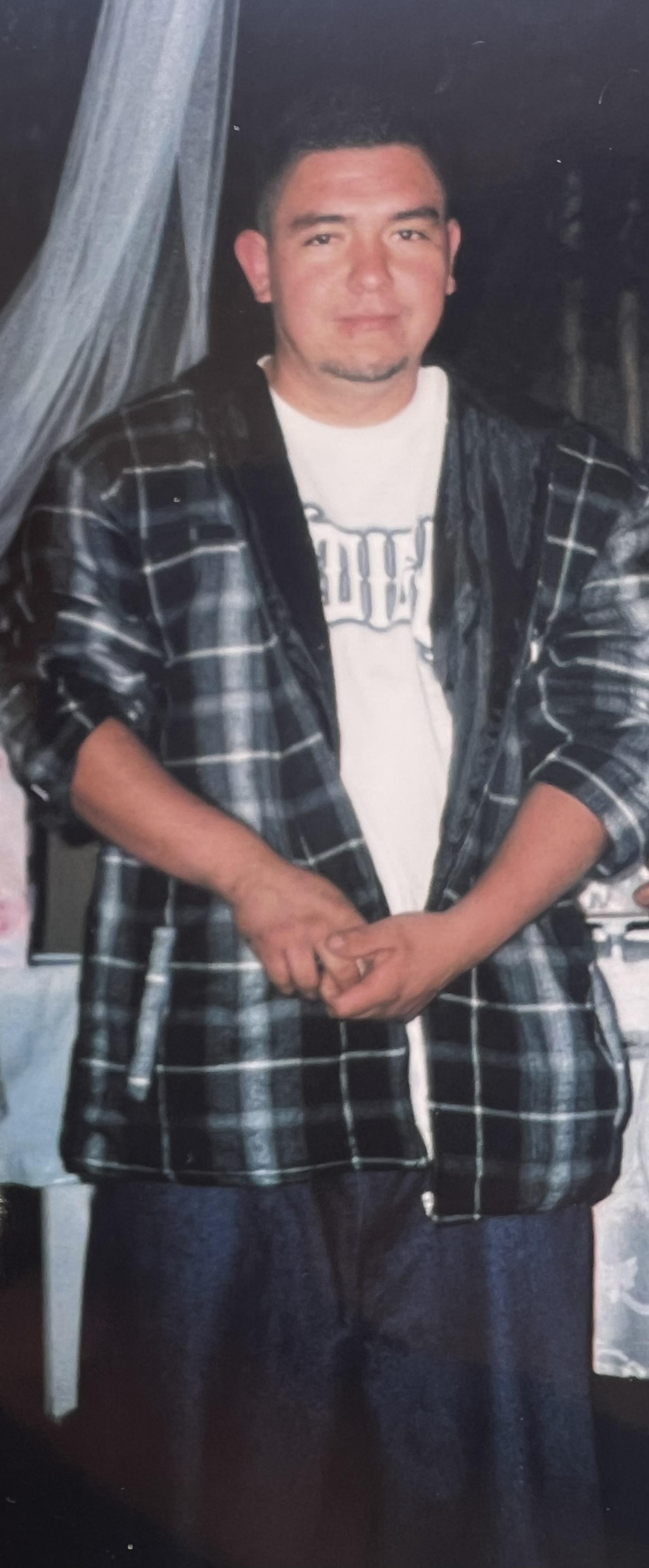 A man in a plaid jacket poses with a neutral expression, set against a cozy background.