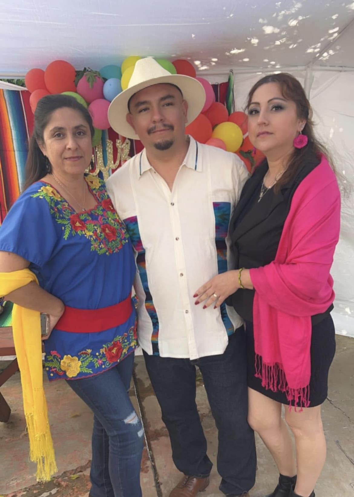 Three people are dressed in vibrant traditional clothing during a festive event with decorations.