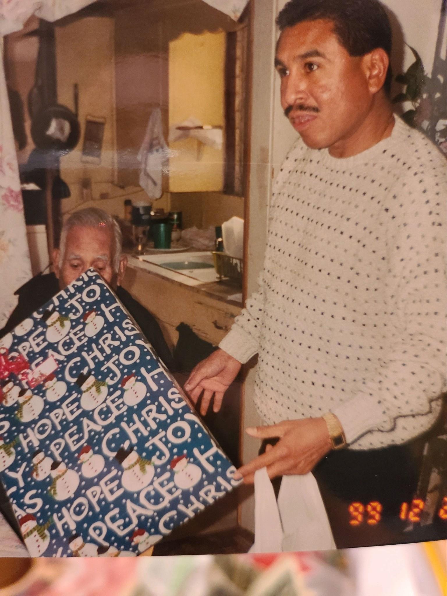 A man presents a wrapped gift to an elderly woman during a family gathering at home.