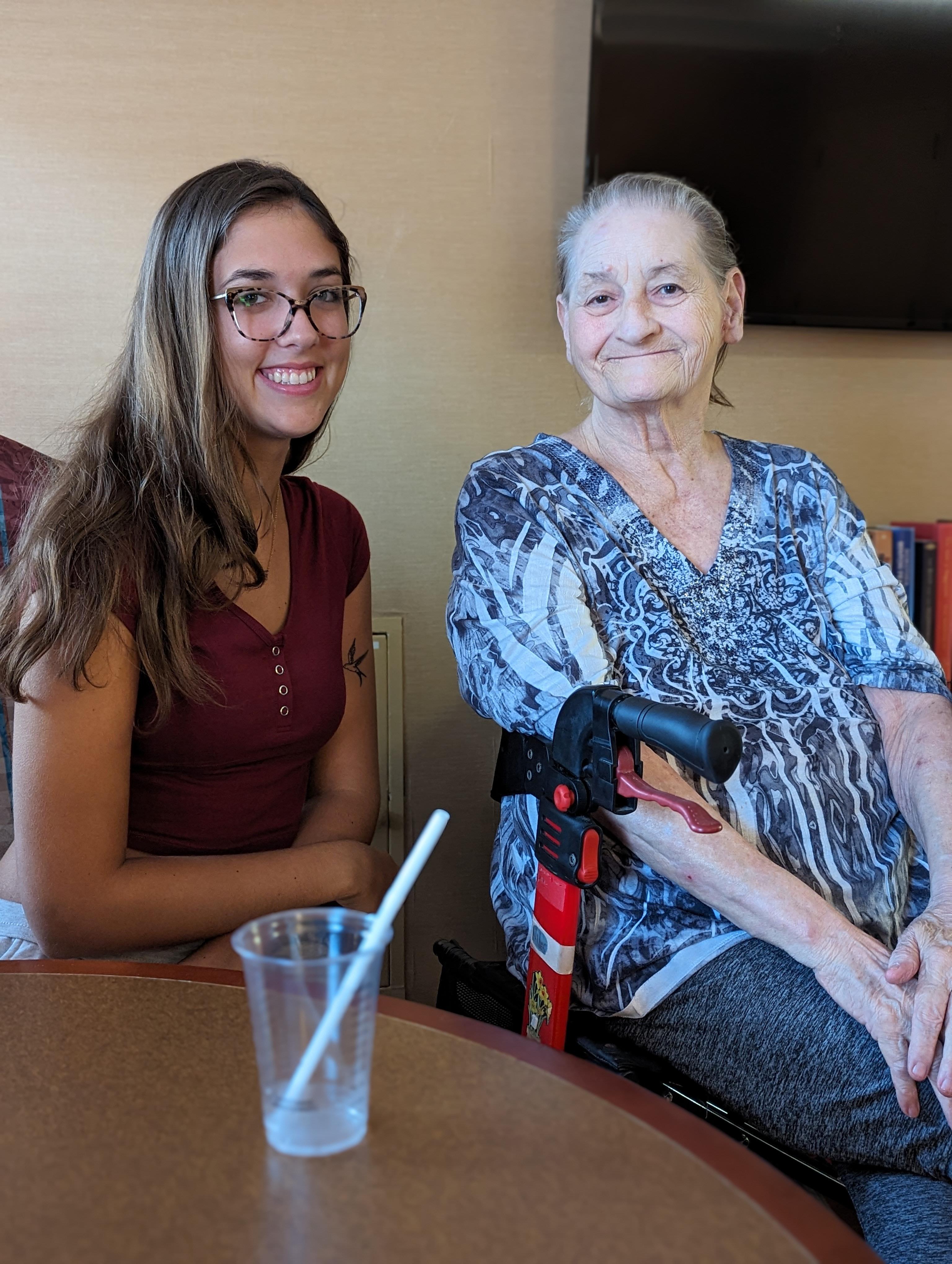 Young woman and elderly woman share a joyful moment indoors, sitting near a table with a drink.