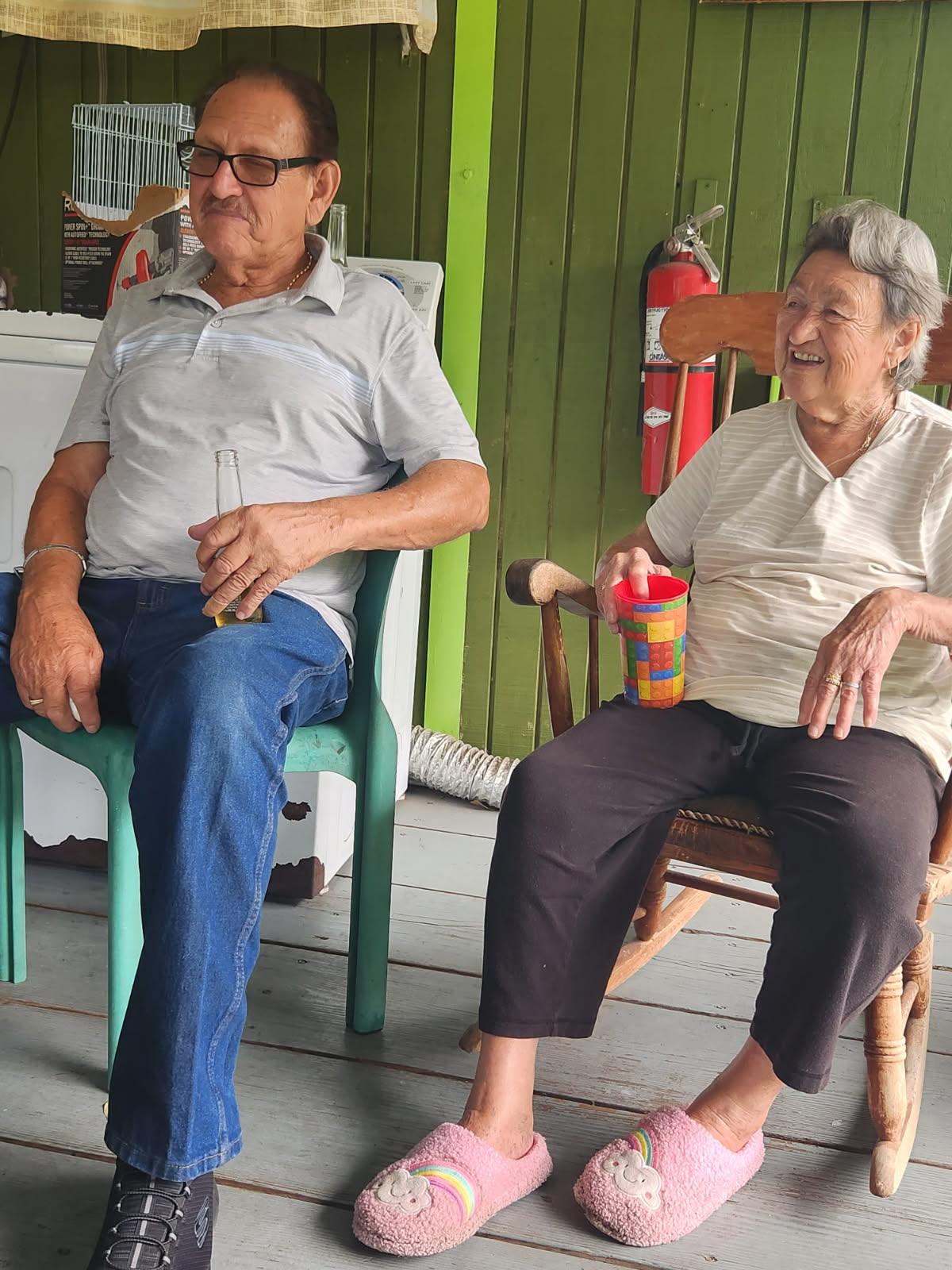 An elderly couple relaxes on the porch, savoring drinks and each other's company.