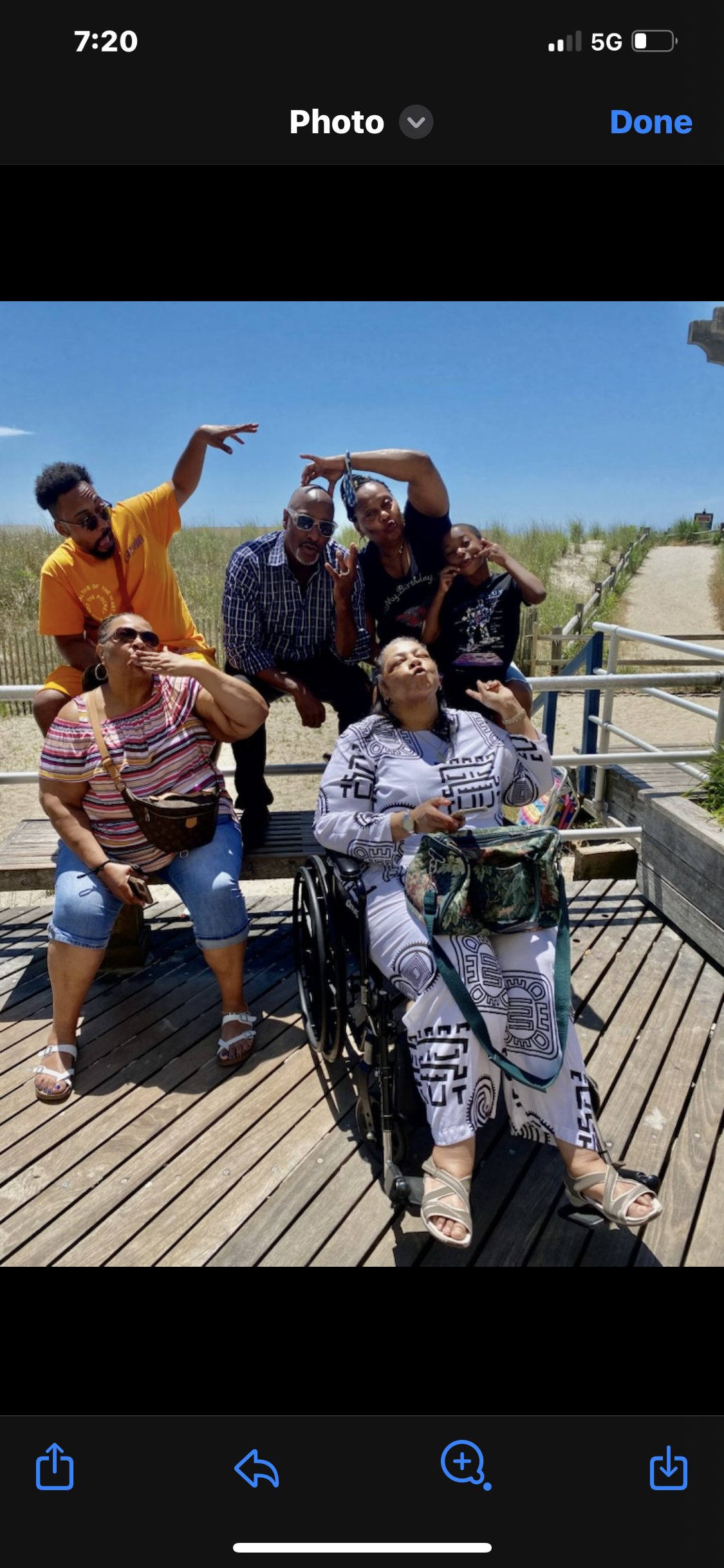 A group of six people pose happily on a wooden boardwalk near a beach, celebrating together.