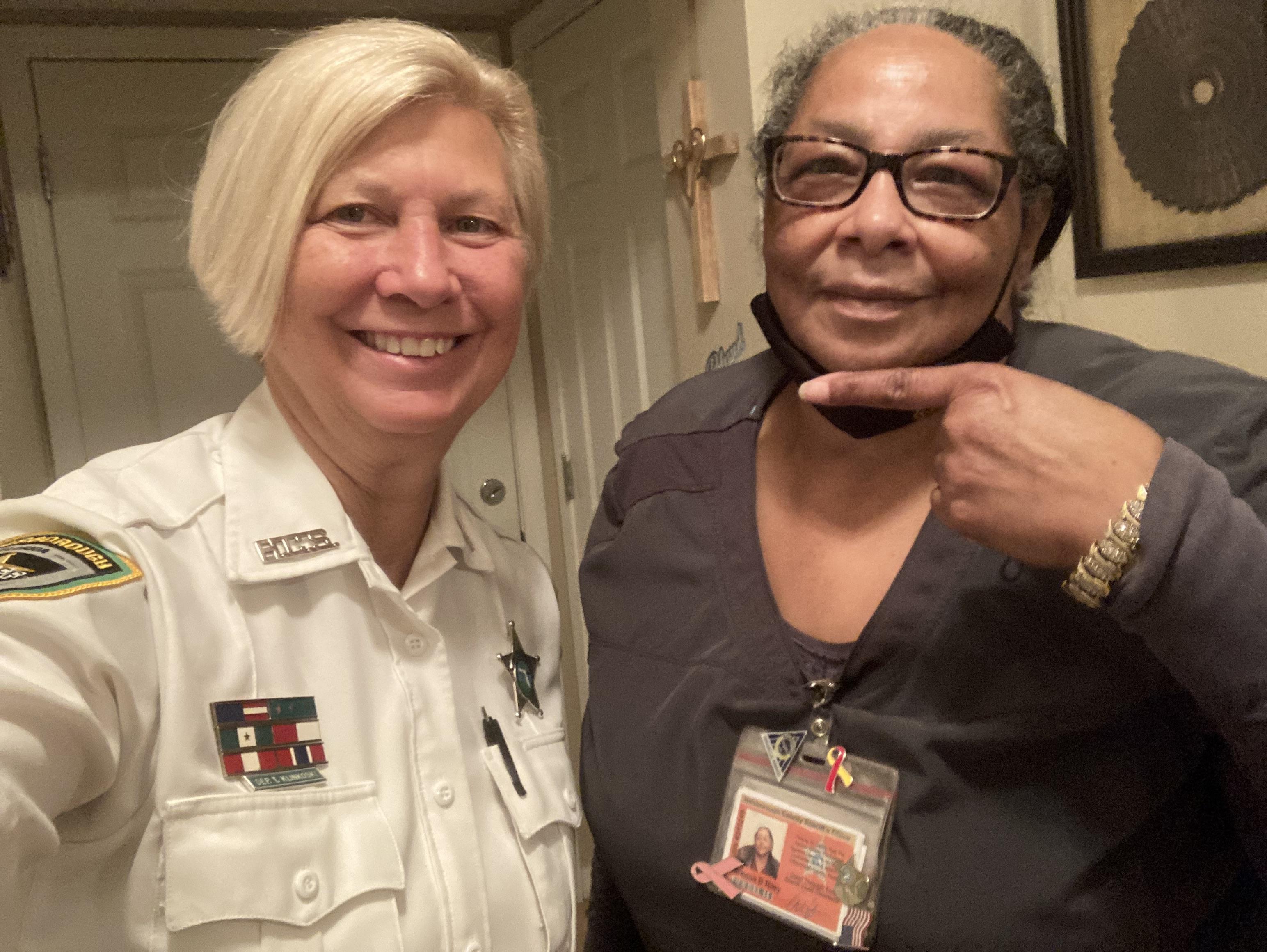 Two women pose together in a home, displaying joy and community spirit through their smiles.