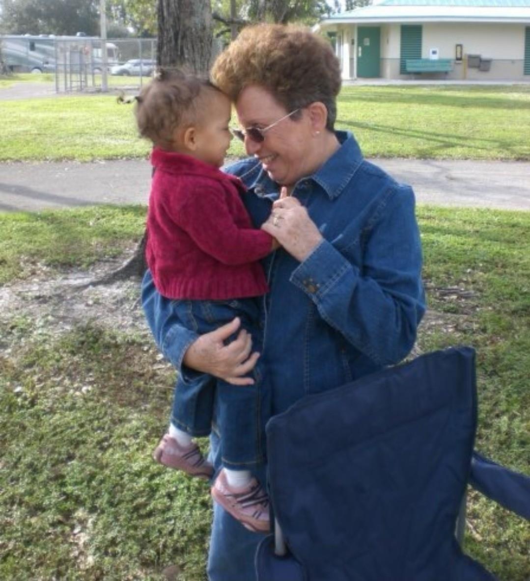 A grandmother shares a delightful moment with her grandchild in a green park, both smiling.