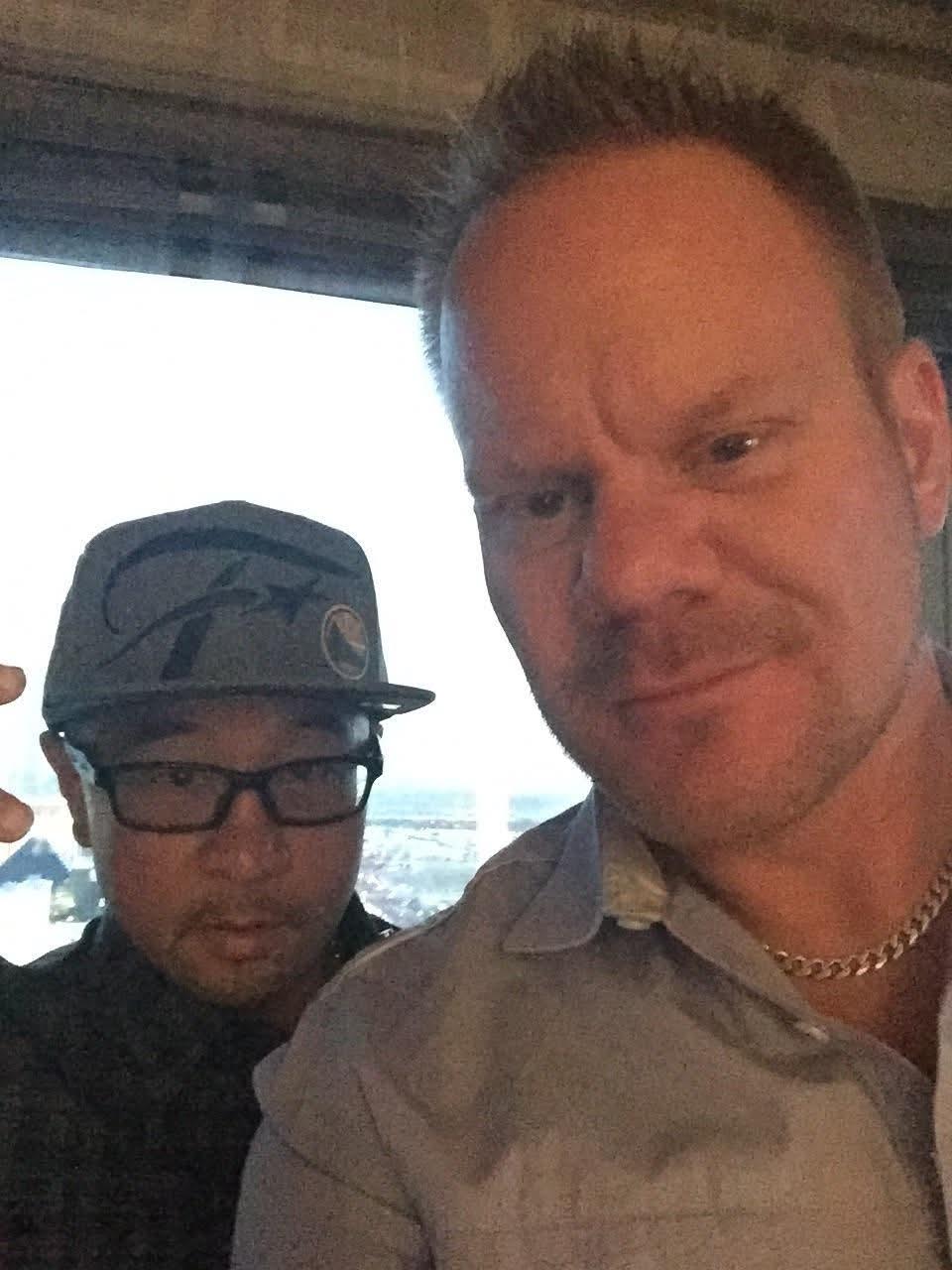 Two friends pose for a selfie with a city skyline visible behind them in the evening.