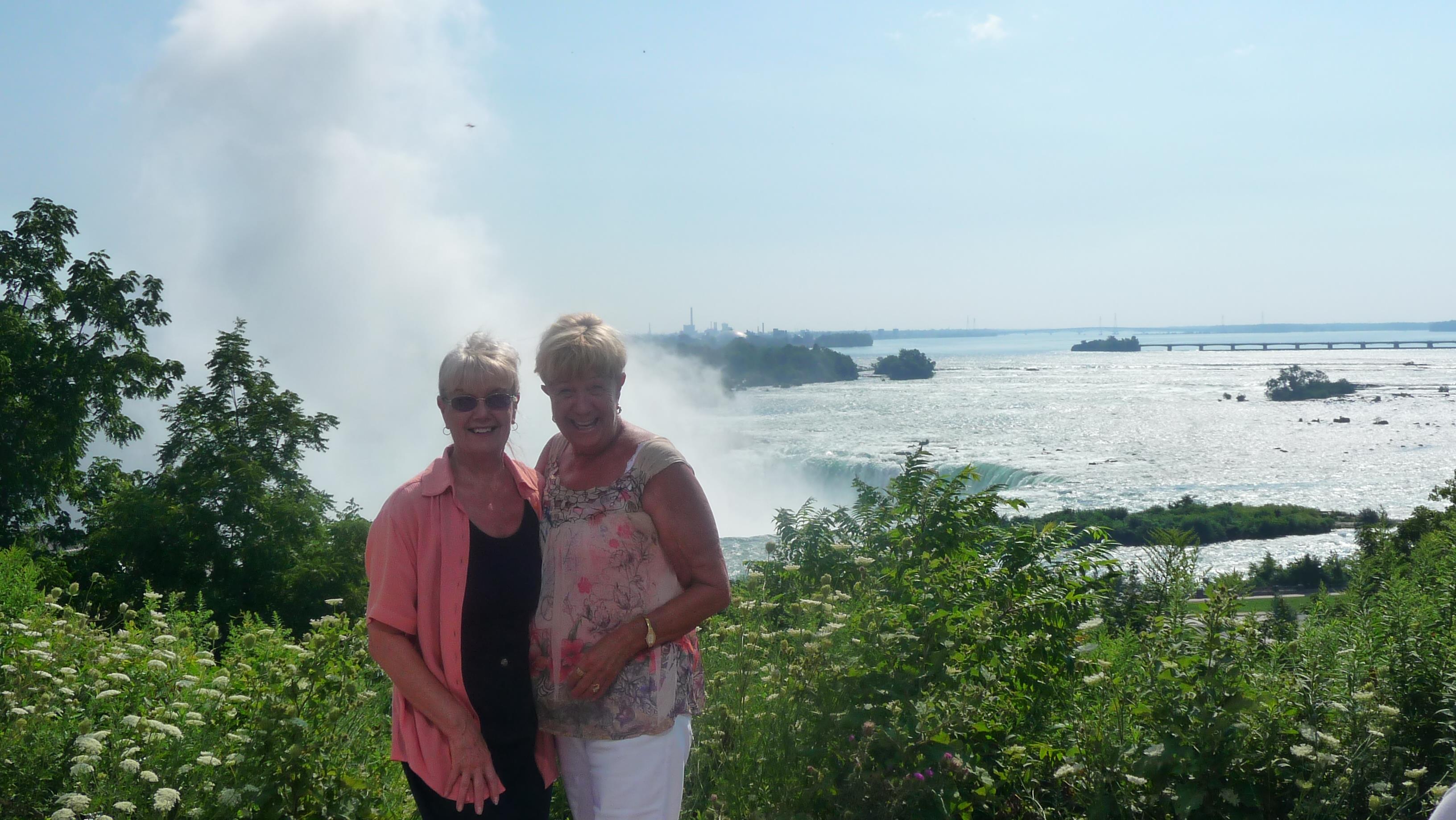 Two women pose happily against the backdrop of a renowned waterfall and river.