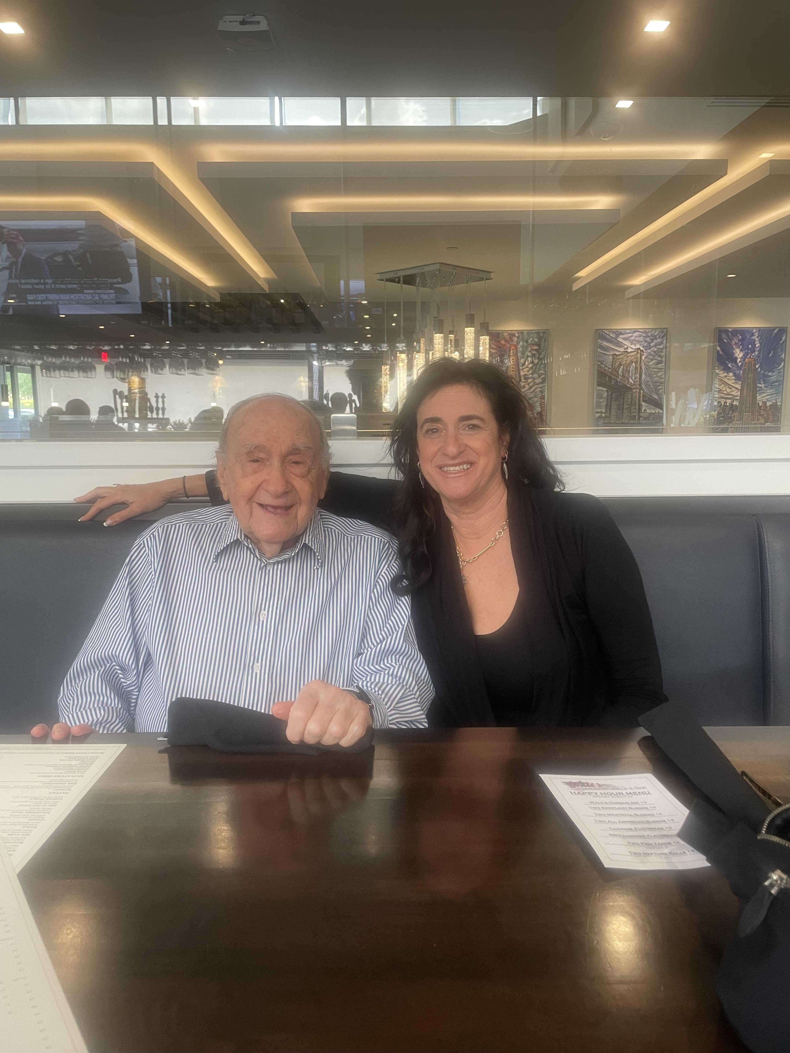 A grandfather and granddaughter share a warm moment together at a restaurant table, smiling happily.
