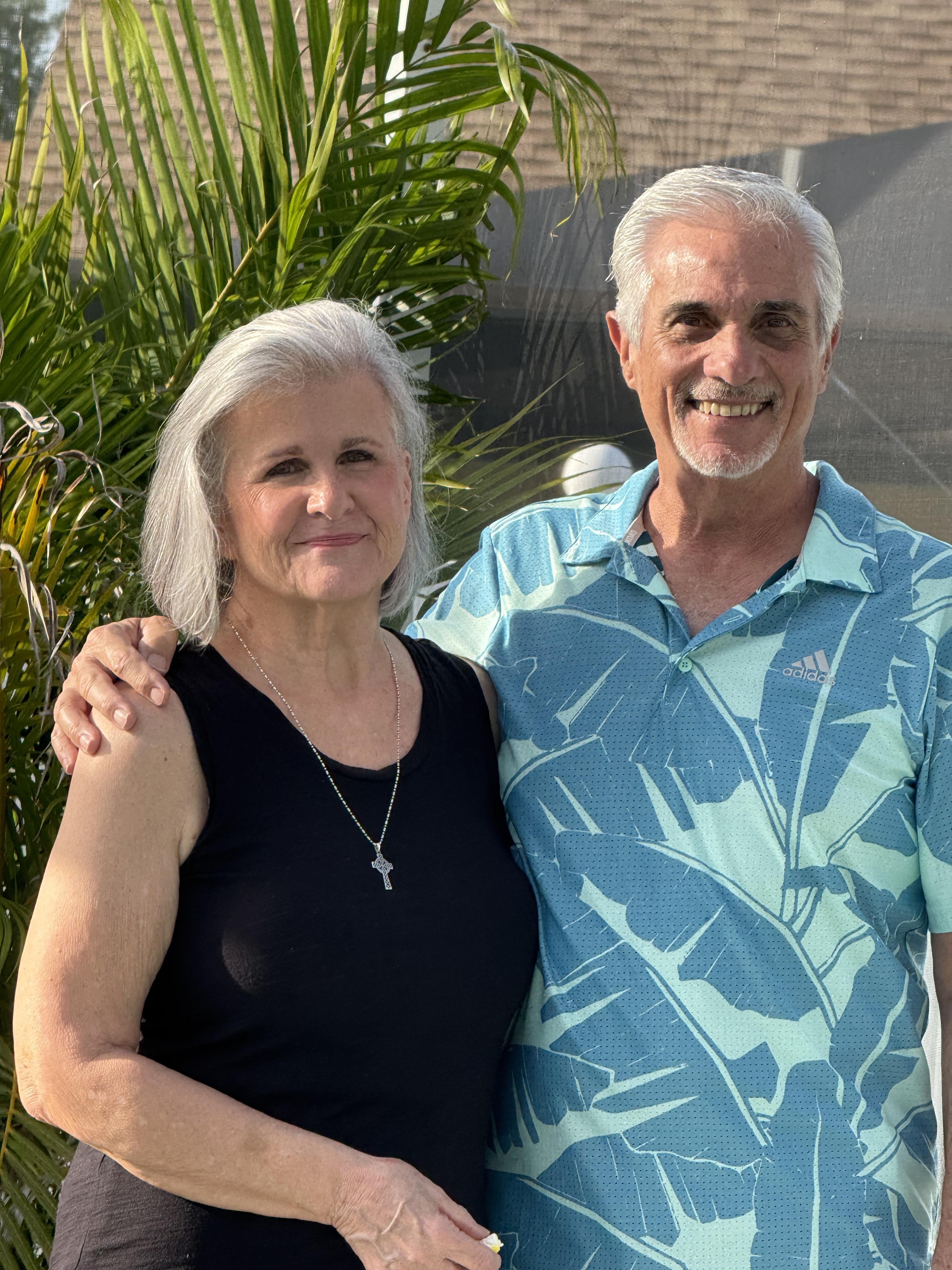 Smiling couple poses happily in a vibrant outdoor setting with tropical plants.