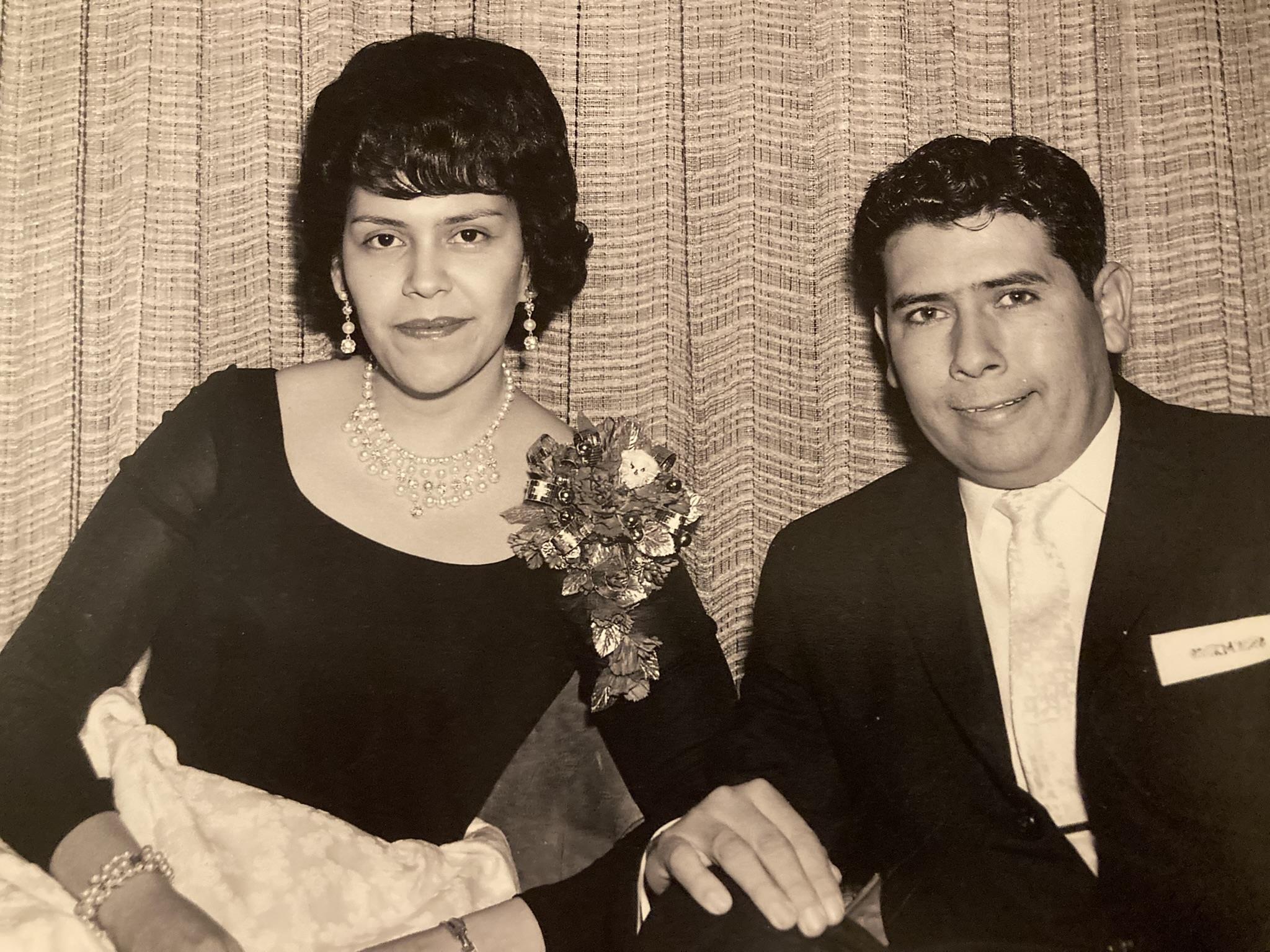 An elegantly dressed couple poses for a portrait at a vintage-themed formal event.