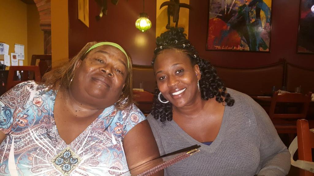 Two friends smile at a table in a lively restaurant, savoring their time together.