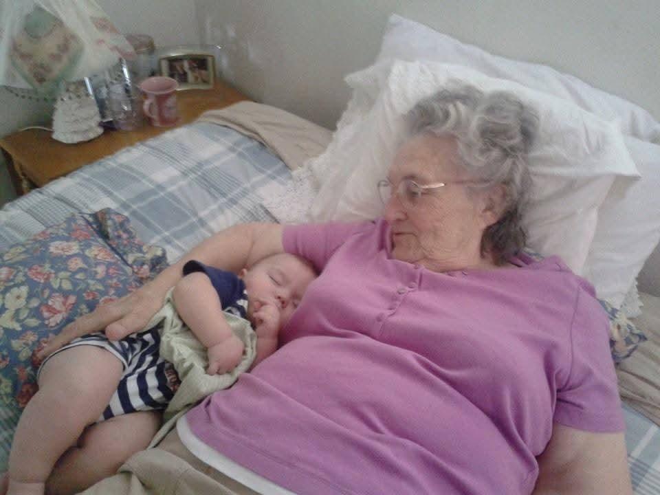 A loving grandmother holds a peaceful baby boy, both enjoying a quiet moment on a bed.