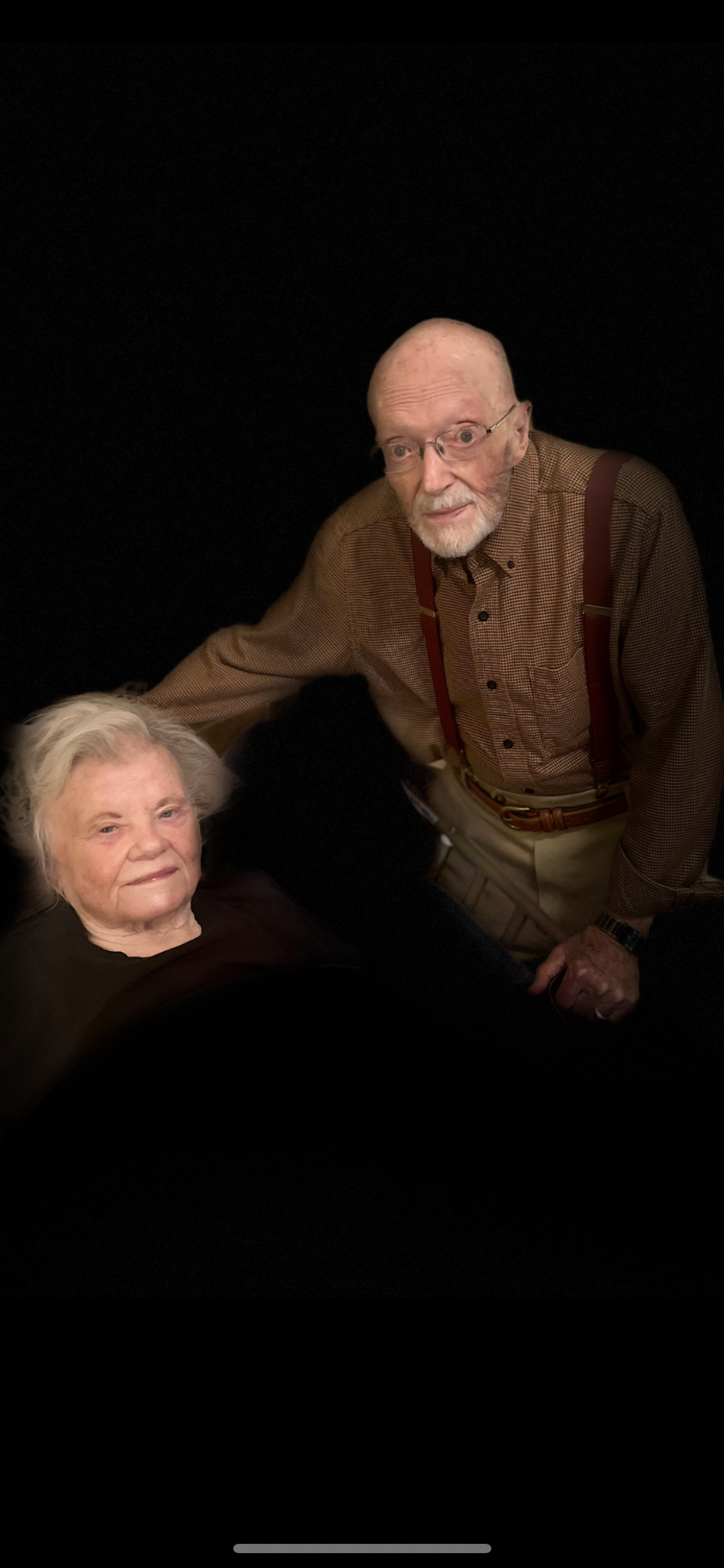 An elderly couple shares a tender moment, expressing warmth and connection in a dimly lit space.