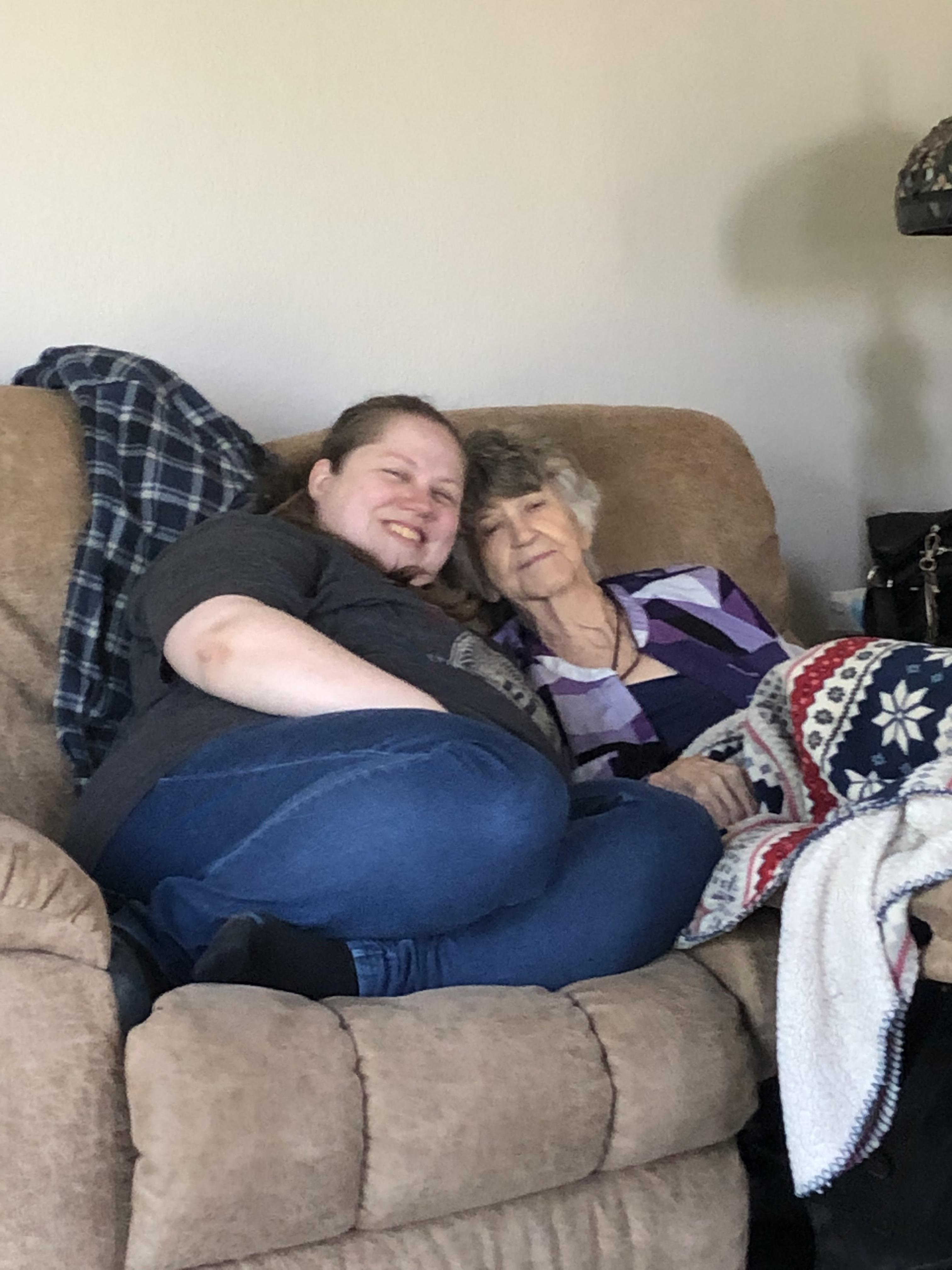 Women relax on a couch, sharing smiles and warmth, showcasing their close bond and love.