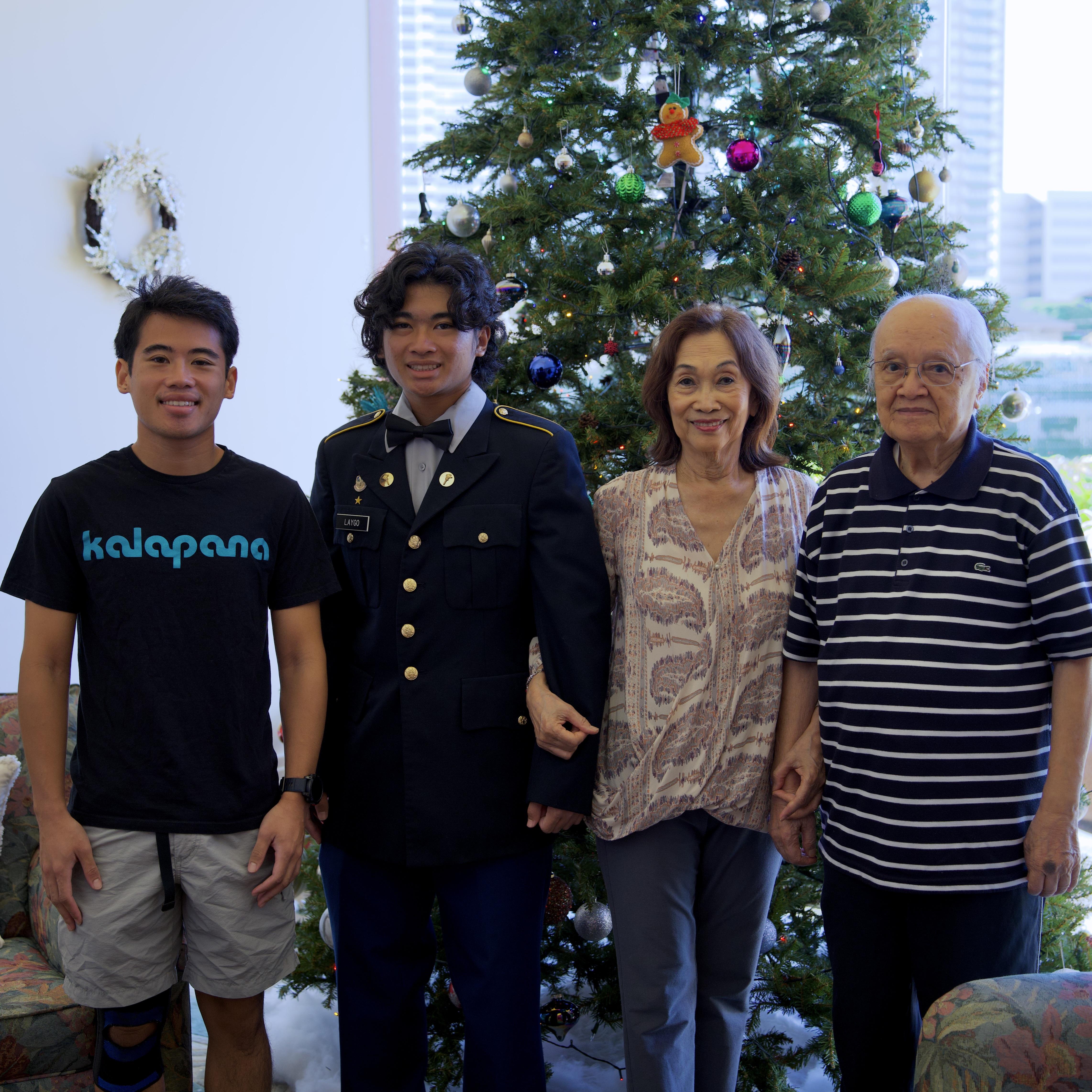Four family members celebrate together by a decorated Christmas tree in a warm, joyful atmosphere.