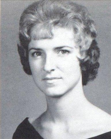 A young woman poses for her yearbook photo, flaunting her curly hair and serious look.