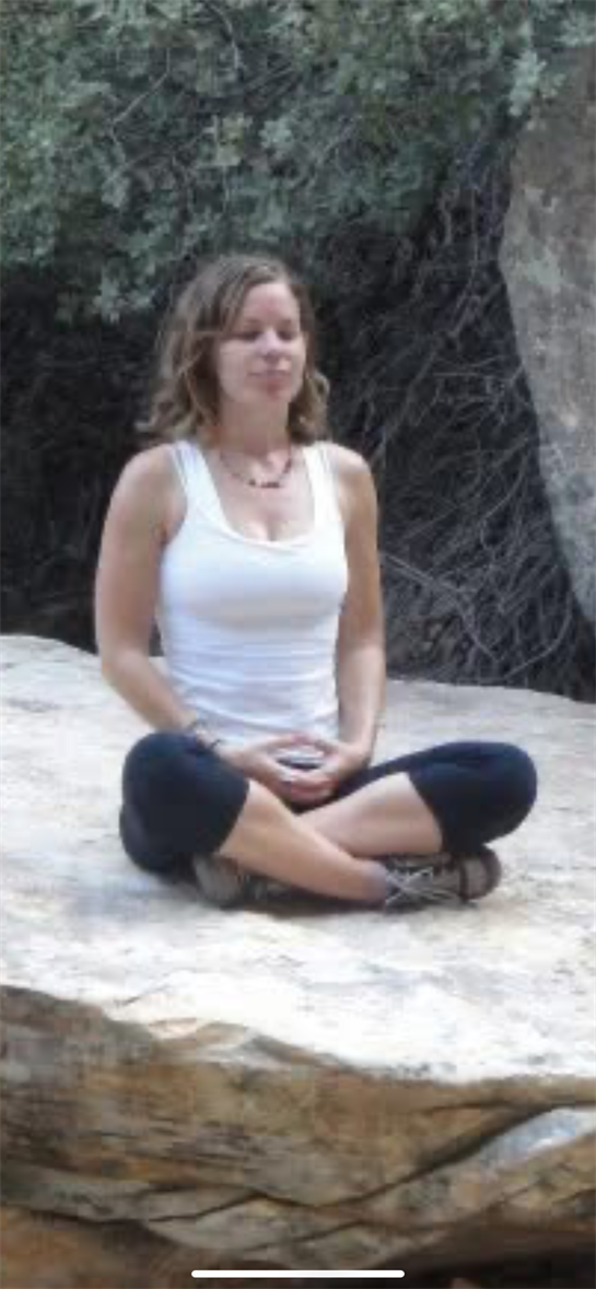 A woman sitting cross legged in a white tank top and black pants