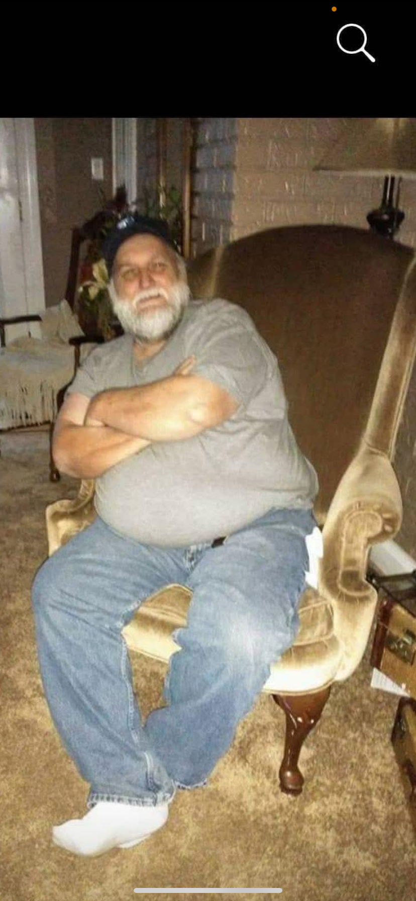 A man relaxes in an armchair with crossed arms in a warm home setting, showcasing comfort.