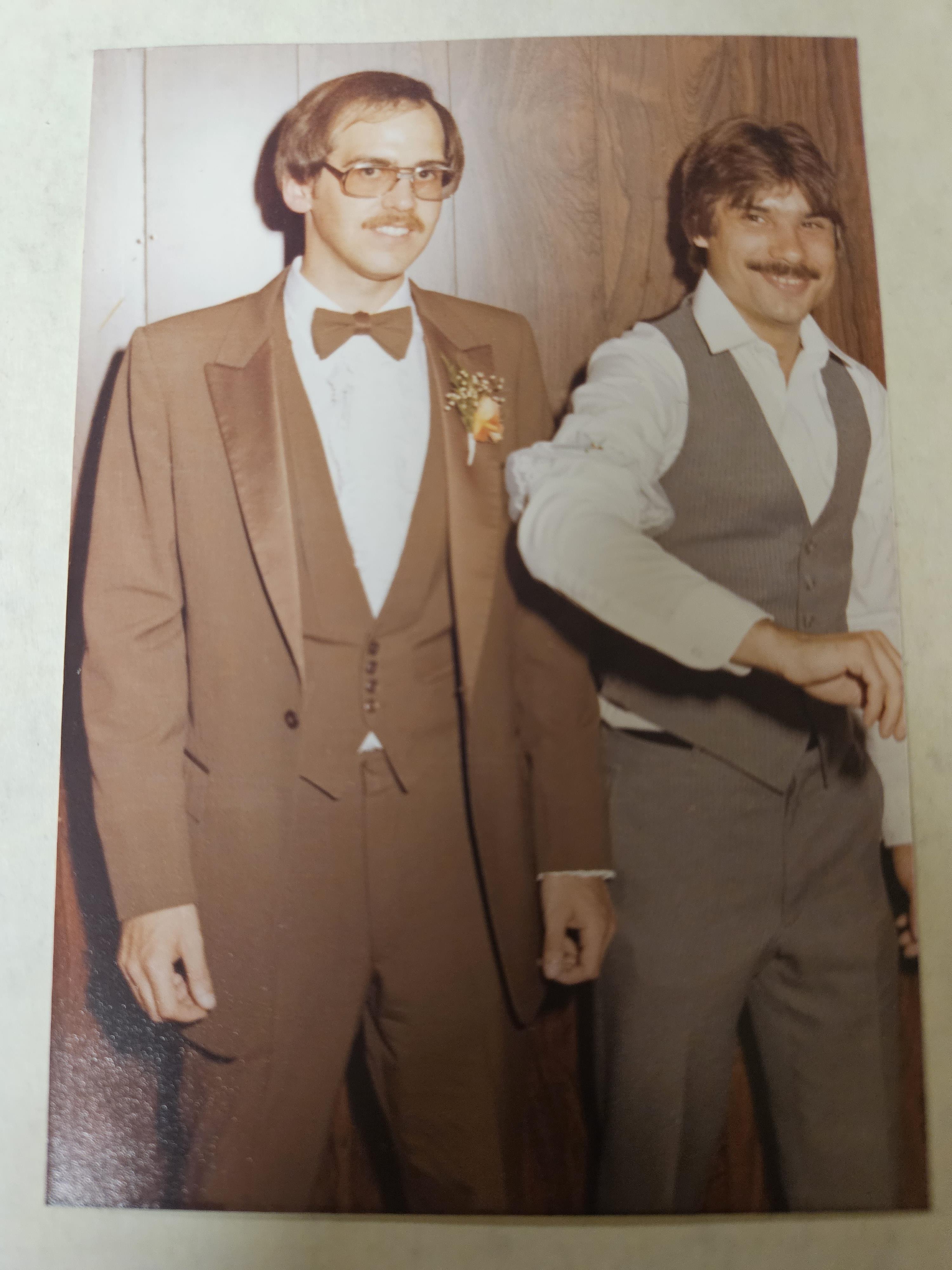 Men with mustaches wear formal suits and stand together in a cozy indoor venue celebrating an event.