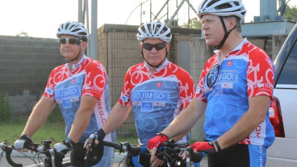Three cyclists in bright jerseys stand with their bikes, ready to start their morning ride together.
