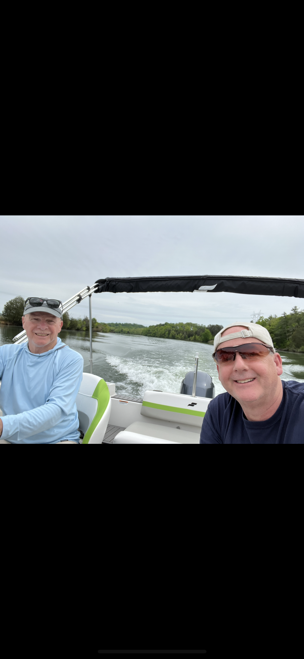 Friends are having a great time on a boat, cruising through a tranquil lake under a gray sky.