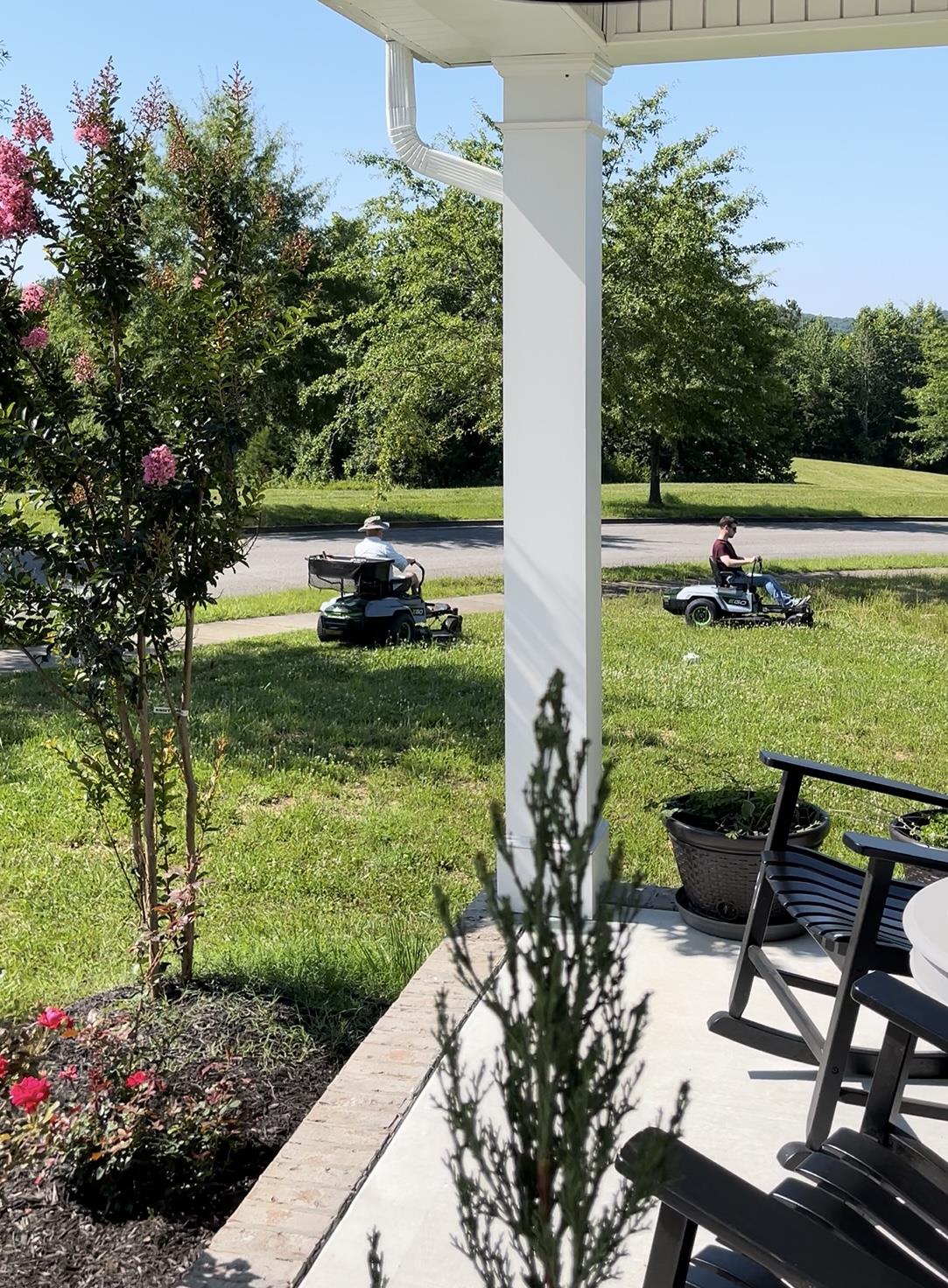 Two individuals are mowing the lawn on a sunny afternoon in a residential neighborhood.
