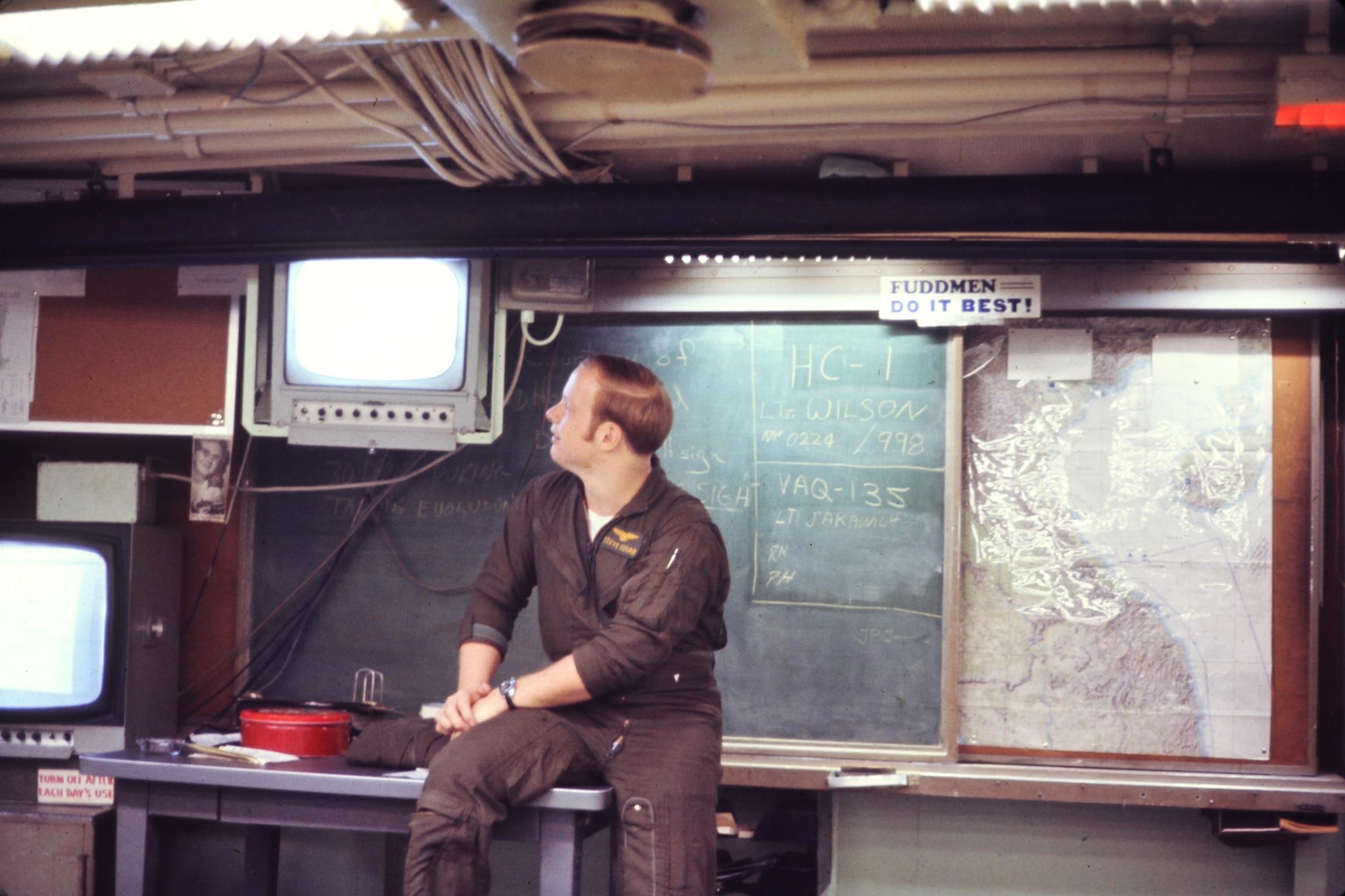 A naval officer monitors multiple screens while seated in a submarine's control room, mid-1970s.