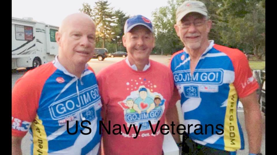 Three Navy veterans celebrate their camaraderie while wearing colorful cycling jerseys outdoors.