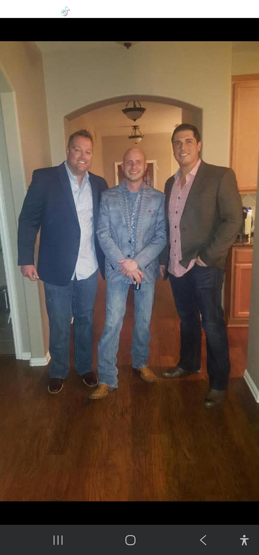 Three men dressed in smart casual attire pose in a cozy home interior during an evening gathering.