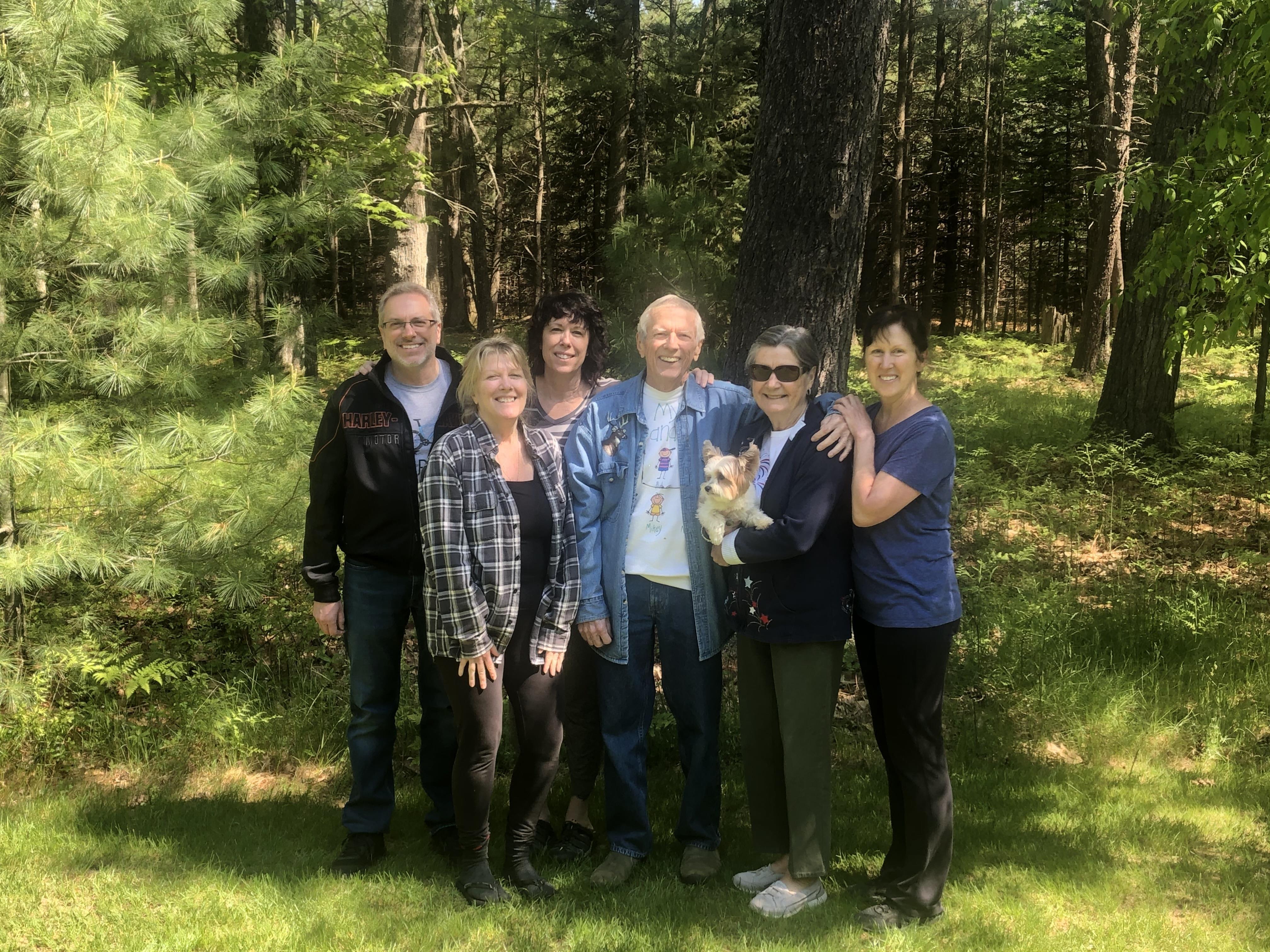 A joyful group of six people poses together in a vibrant forest enjoying their time.